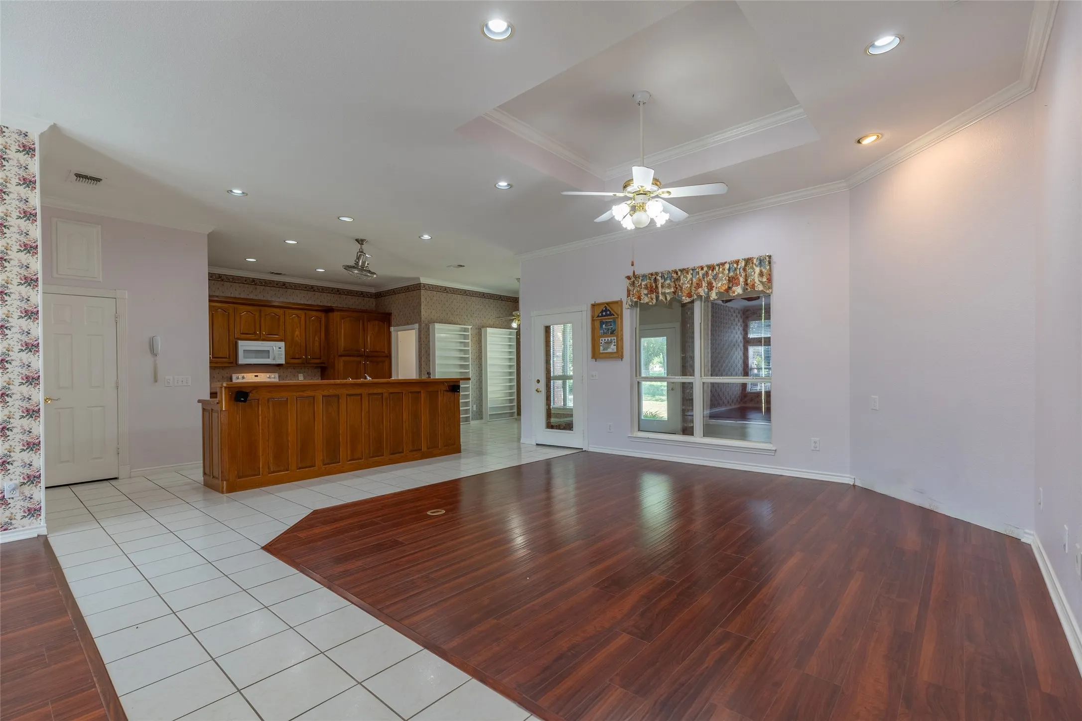 Unfurnished living room featuring light wood-style flooring, crown molding, recessed lighting, ceiling fan, and a raised ceiling