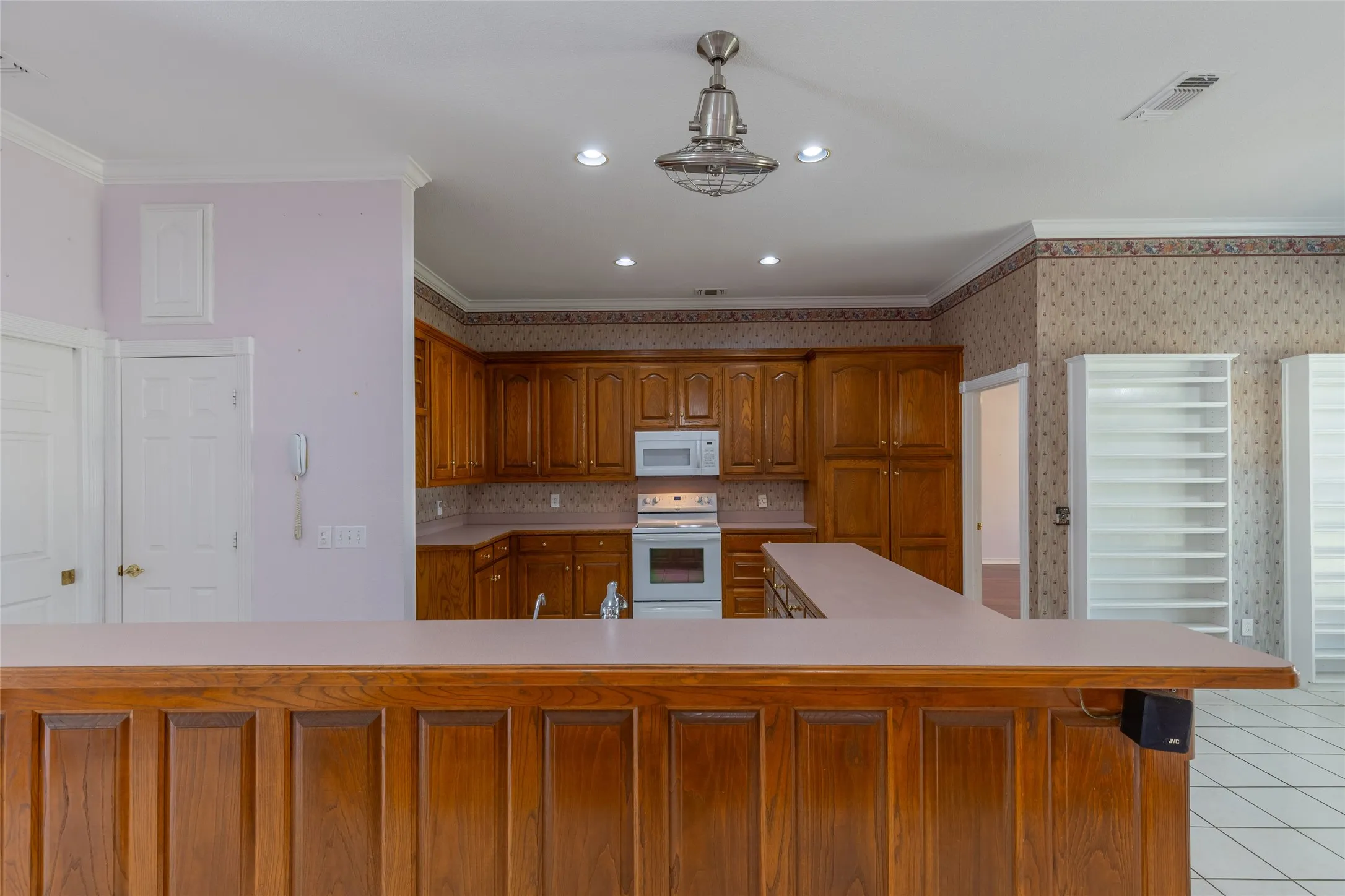 Kitchen featuring brown cabinetry, white appliances, ornamental molding, recessed lighting, and light countertops