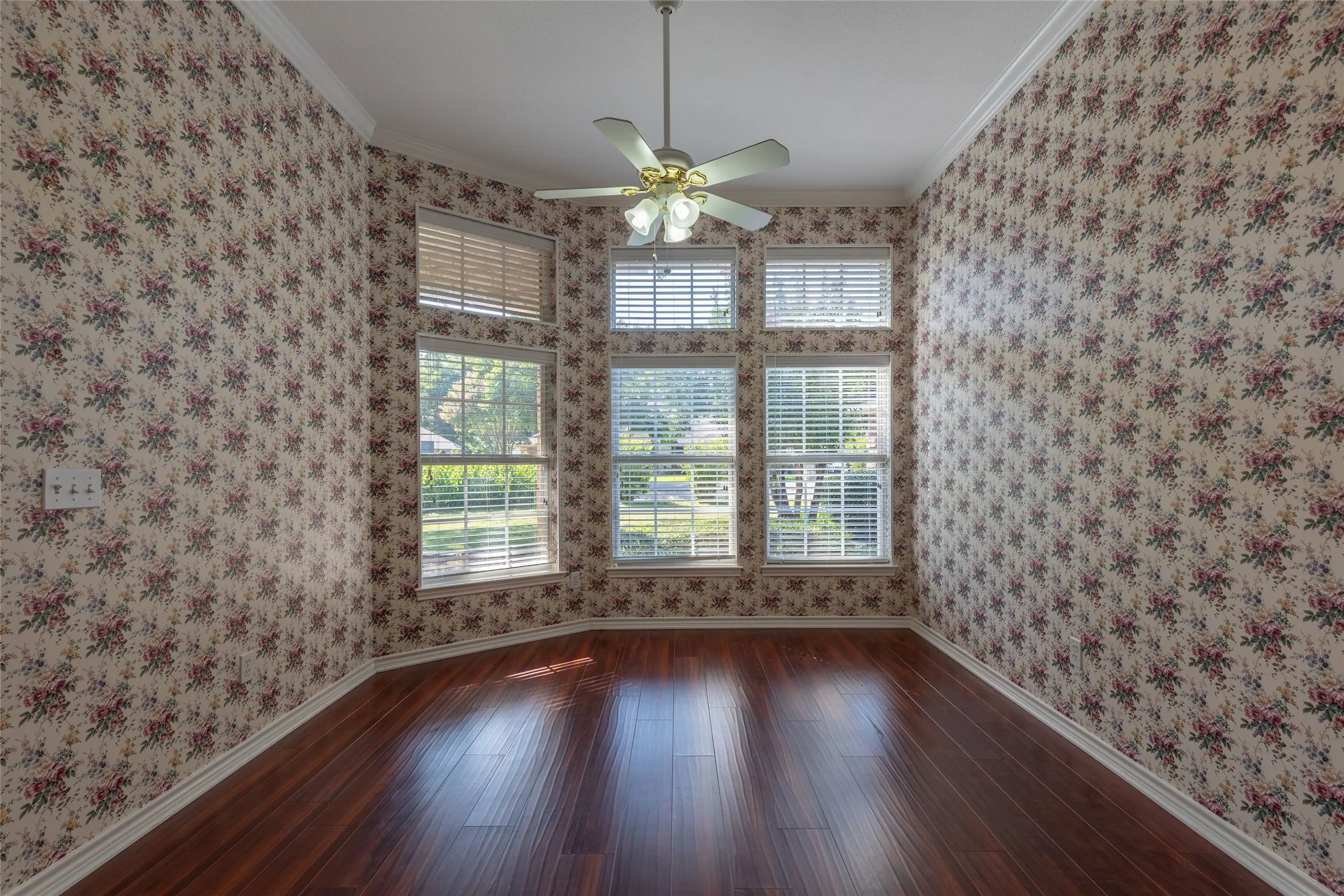 Empty room with crown molding, wallpapered walls, wood finished floors, and ceiling fan