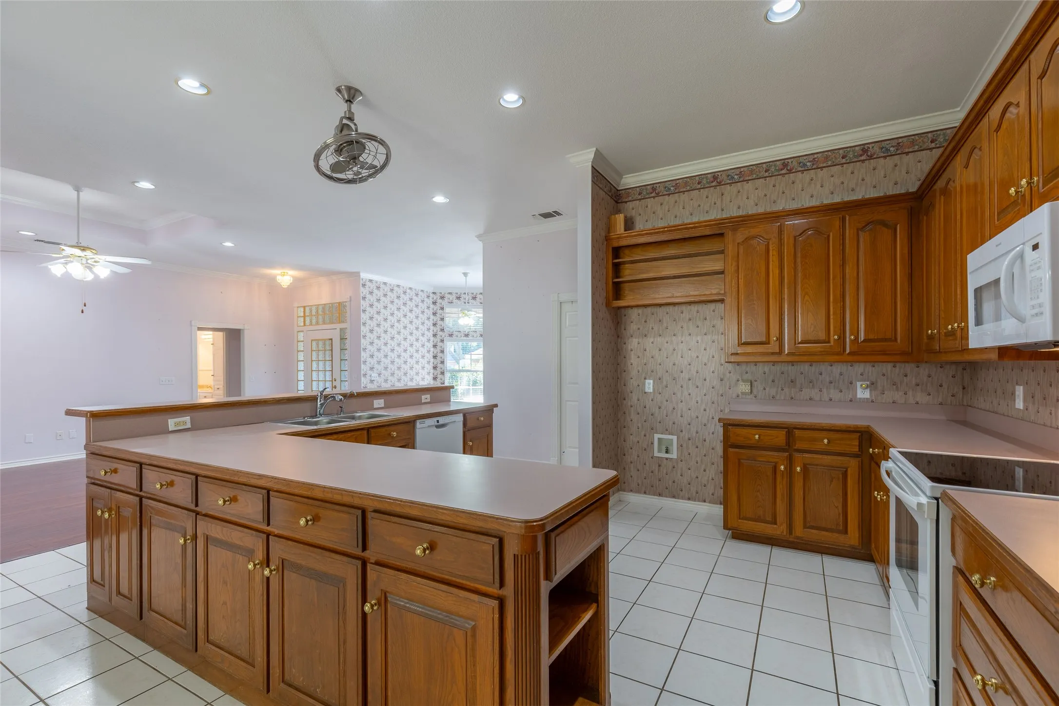Kitchen with ornamental molding, white appliances, recessed lighting, open shelves, and brown cabinetry