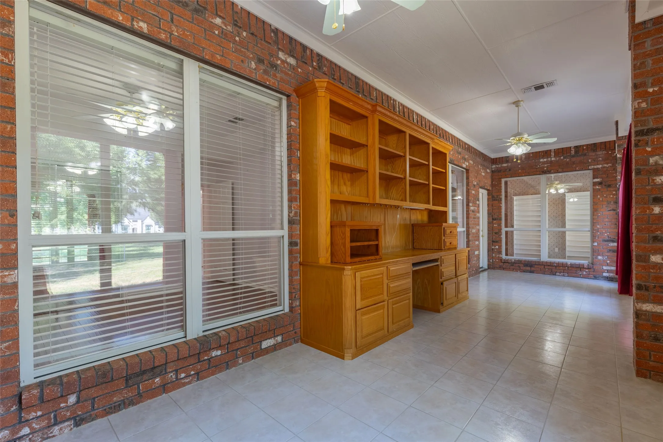 Unfurnished office featuring brick wall, ceiling fan, built in study area, crown molding, and light tile patterned flooring