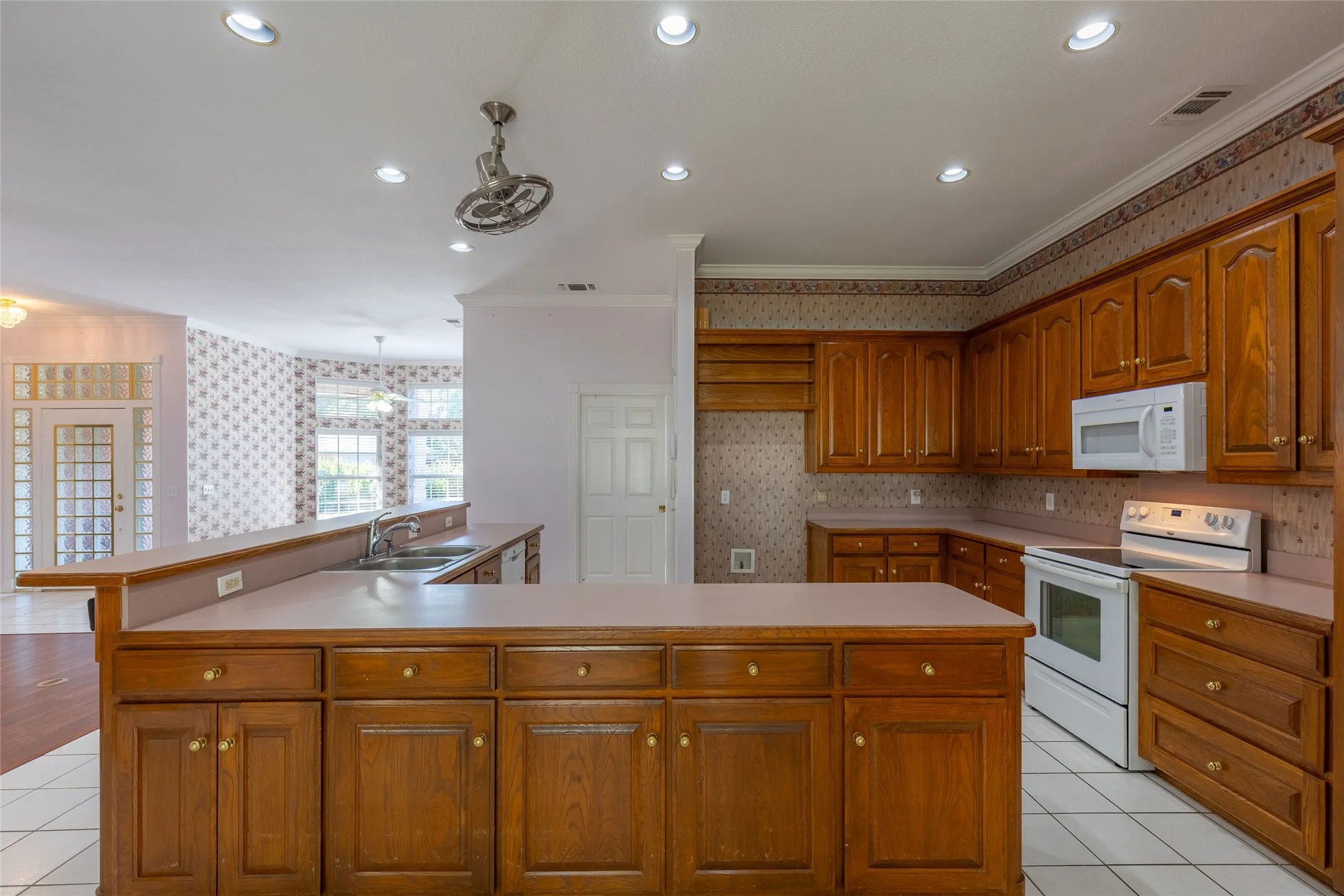 Kitchen featuring wallpapered walls, white appliances, light tile patterned floors, brown cabinets, and crown molding