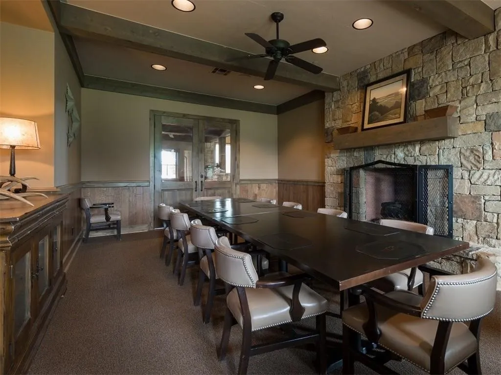 Carpeted dining room with a wainscoted wall, ceiling fan, beam ceiling, a stone fireplace, and recessed lighting