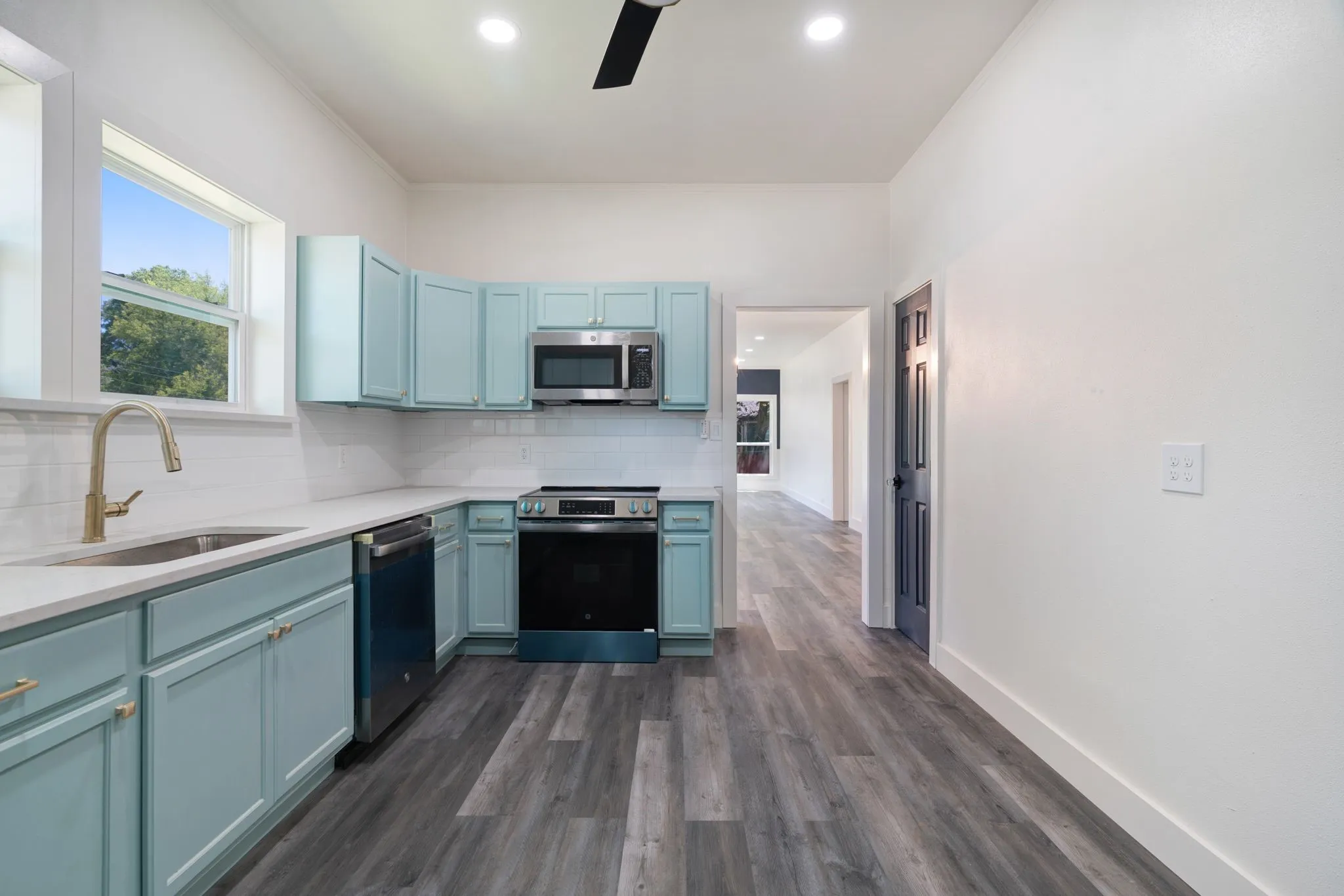 Kitchen with ceiling fan, tasteful backsplash, blue cabinets, stainless steel appliances, and dark wood-style flooring
