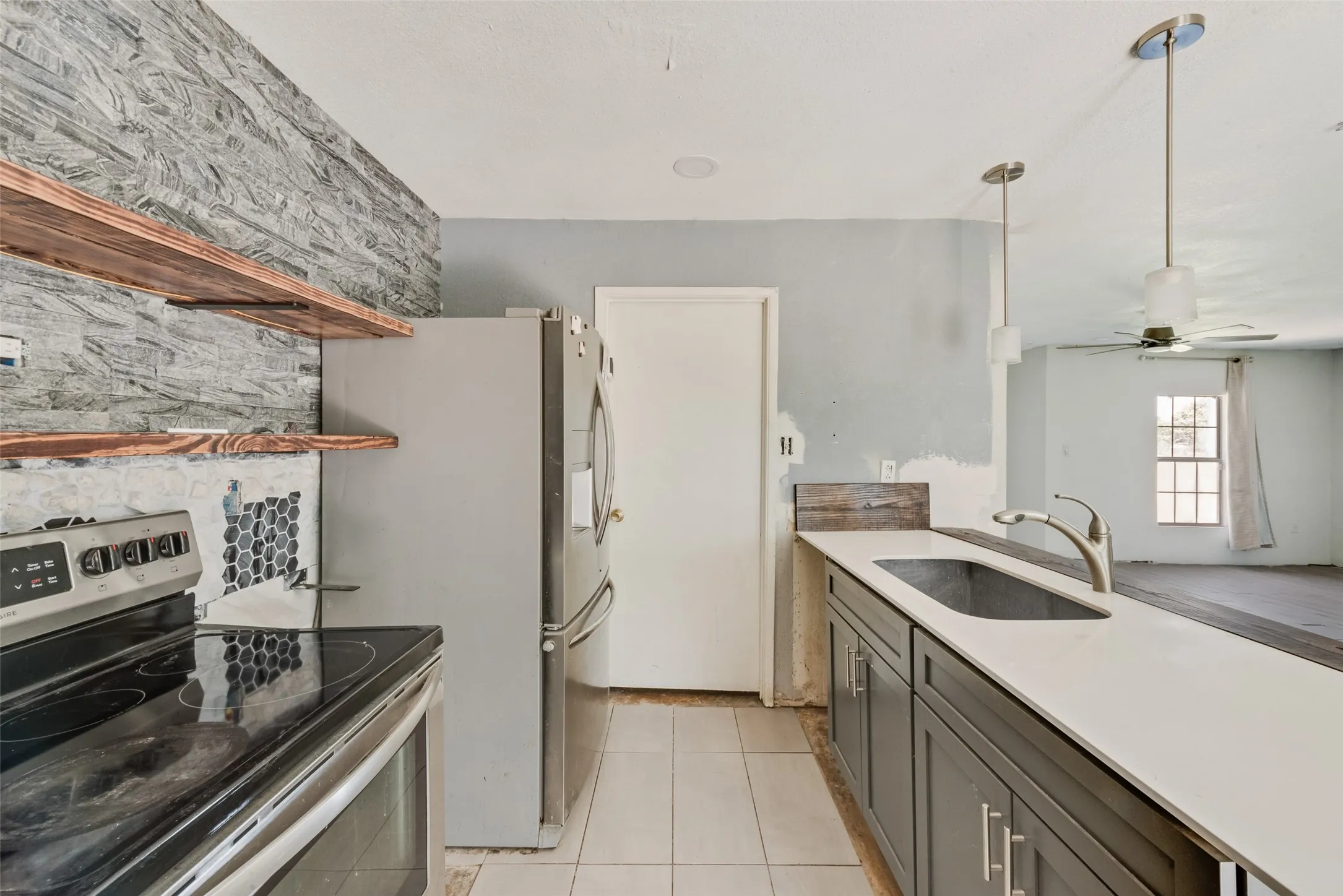 Kitchen with stainless steel electric stove, ceiling fan, light tile patterned floors, light countertops, and gray cabinets