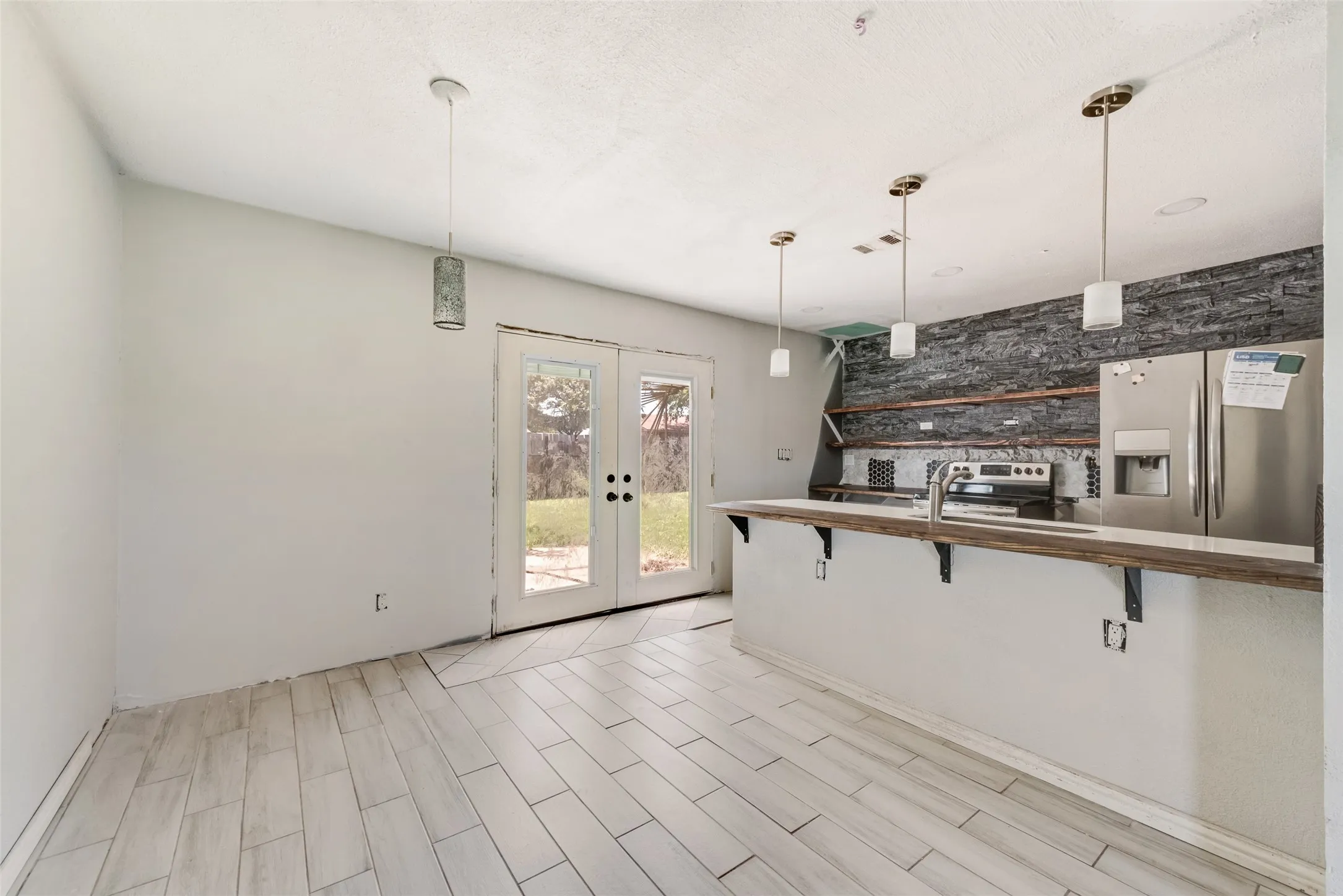 Kitchen featuring french doors, appliances with stainless steel finishes, a breakfast bar, and pendant lighting