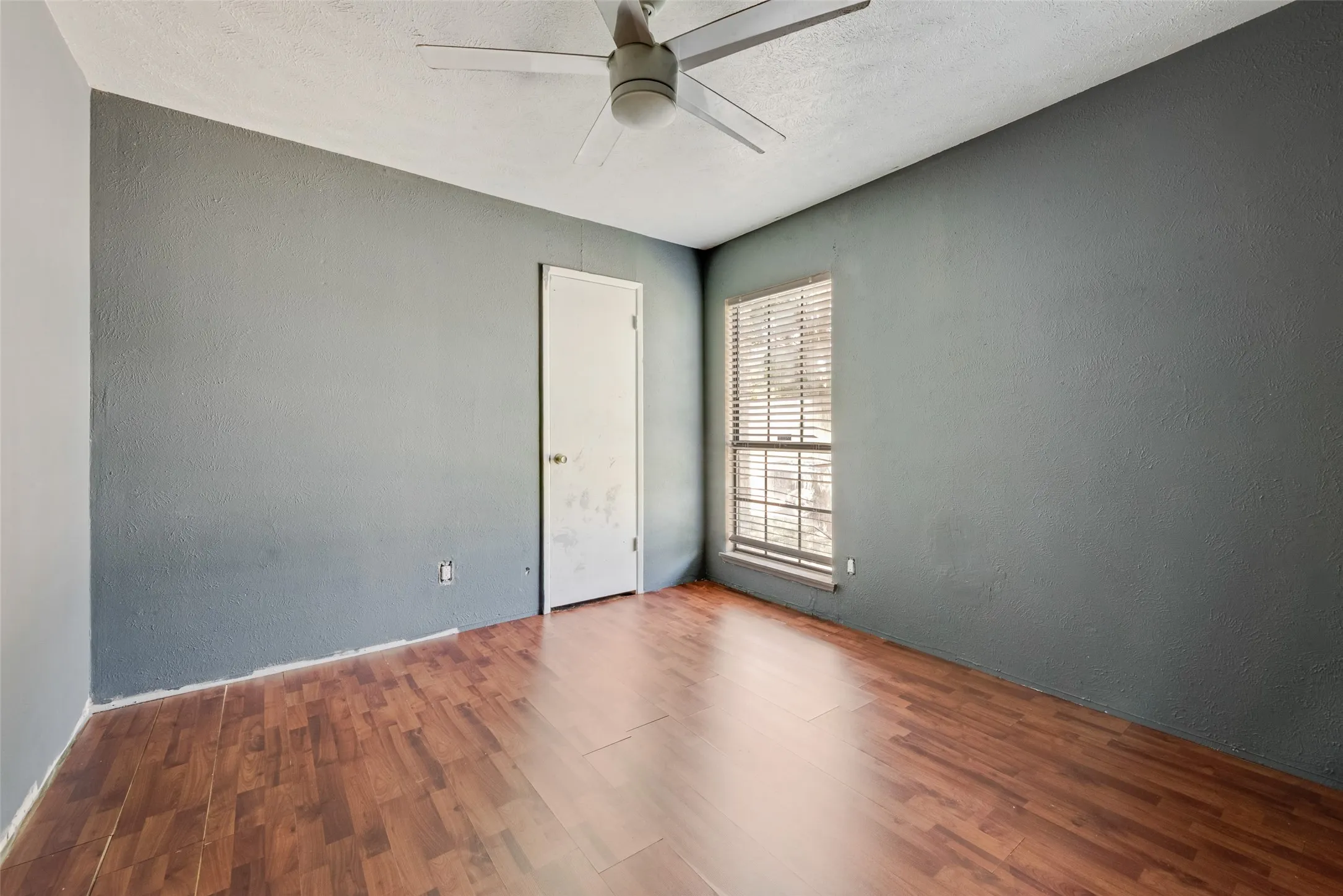 Unfurnished room featuring a ceiling fan, wood finished floors, and a textured wall