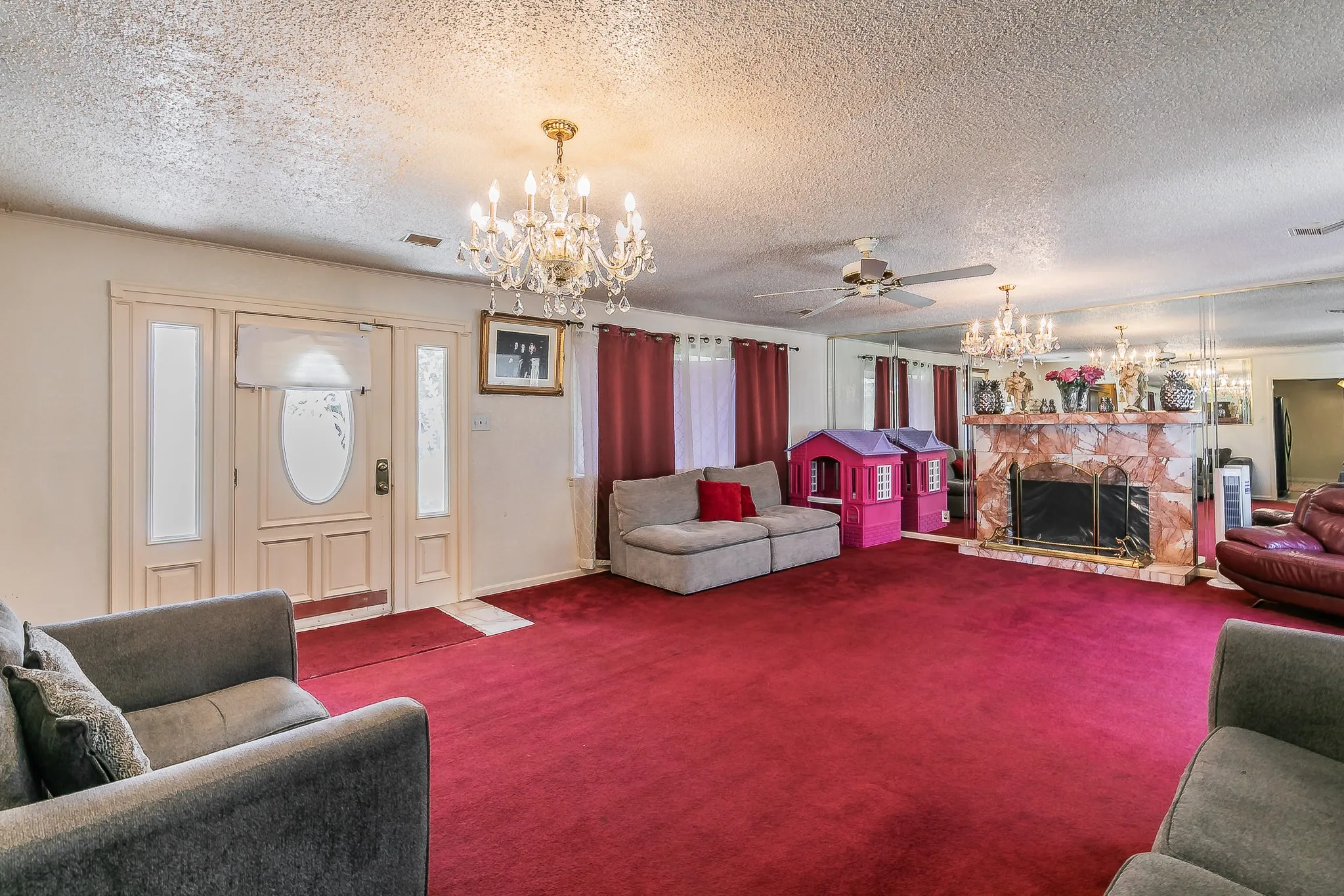 Living room with a chandelier, carpet, a textured ceiling, a ceiling fan, and a stone fireplace