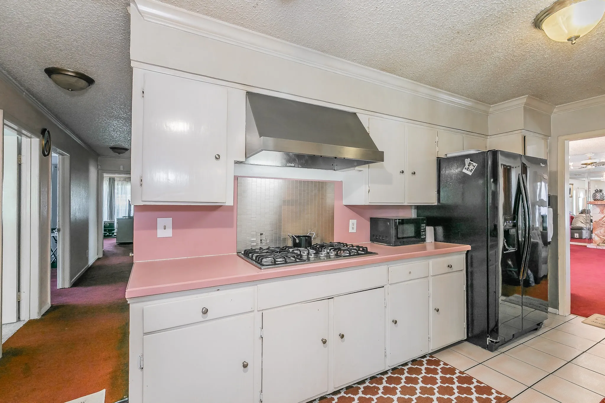 Kitchen featuring a textured ceiling, premium range hood, crown molding, light countertops, and black appliances
