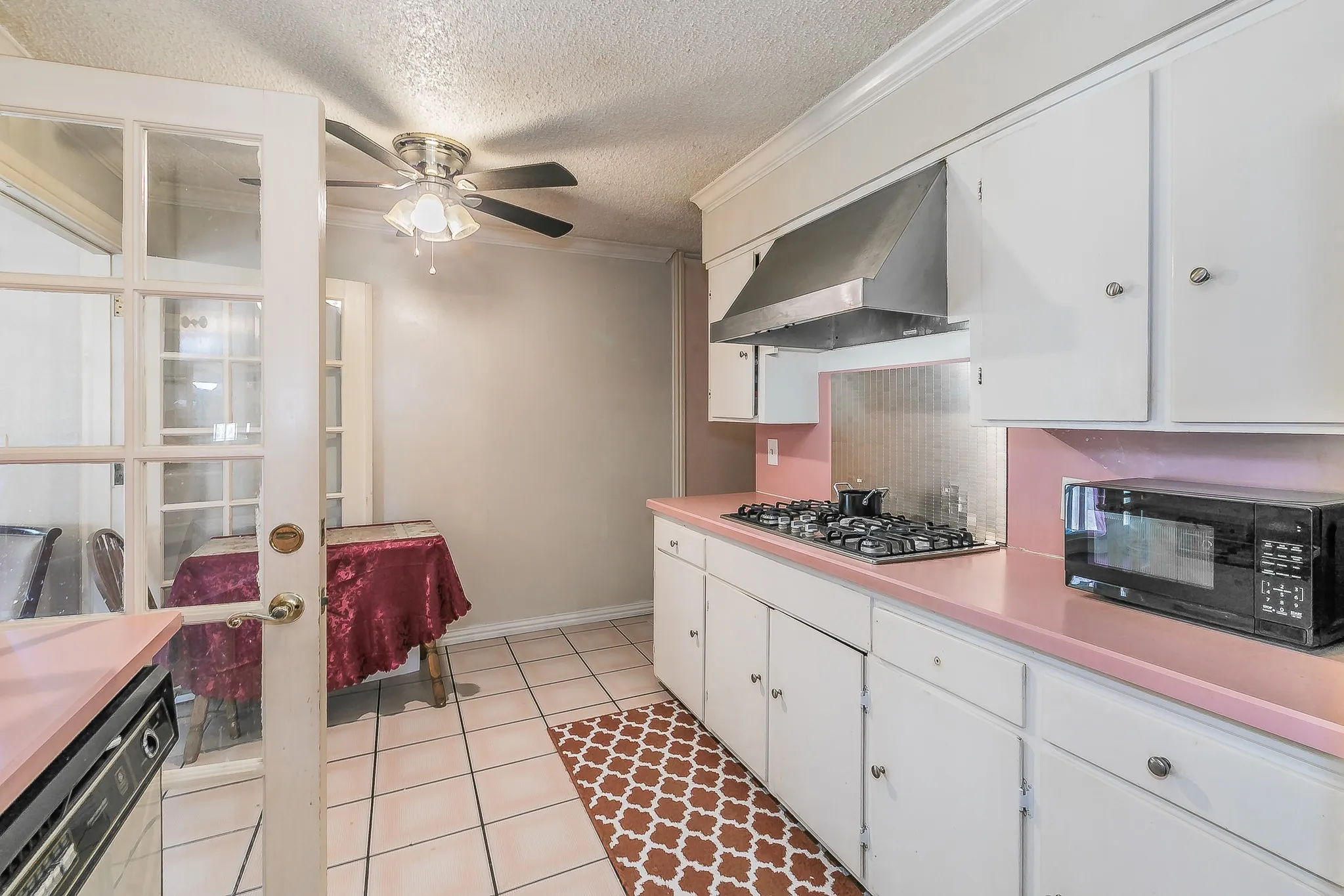 Kitchen featuring dishwasher, black microwave, ceiling fan, wall chimney range hood, and a textured ceiling