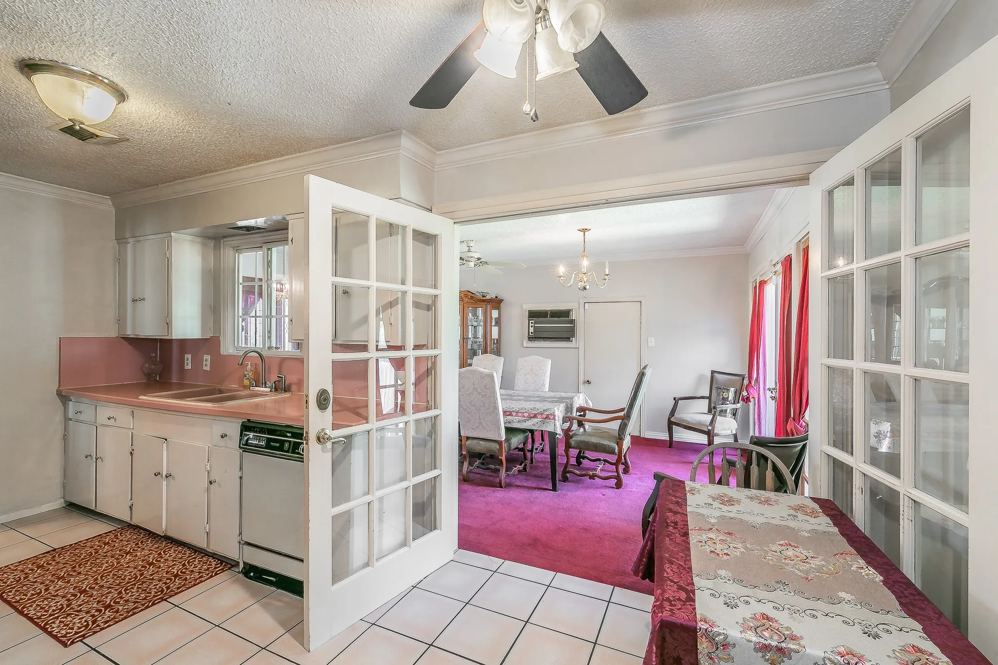 Kitchen featuring a ceiling fan, light tile patterned flooring, light colored carpet, dishwasher, and ornamental molding