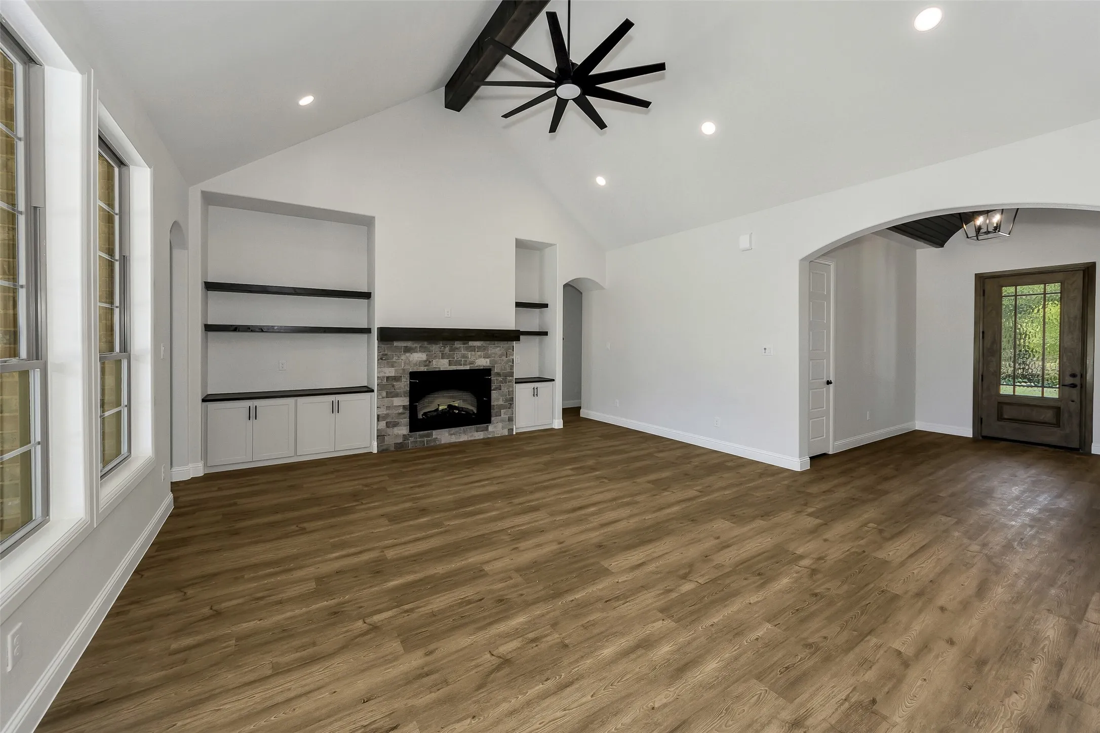 Unfurnished living room featuring beamed ceiling, arched walkways, wood finished floors, a ceiling fan, and a fireplace