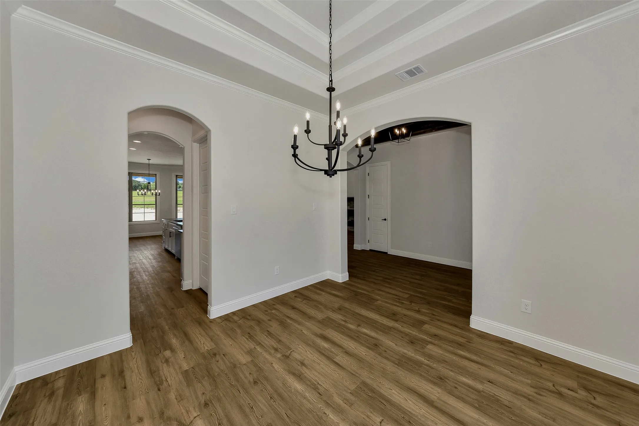 Unfurnished dining area with arched walkways, a chandelier, ornamental molding, wood finished floors, and a tray ceiling