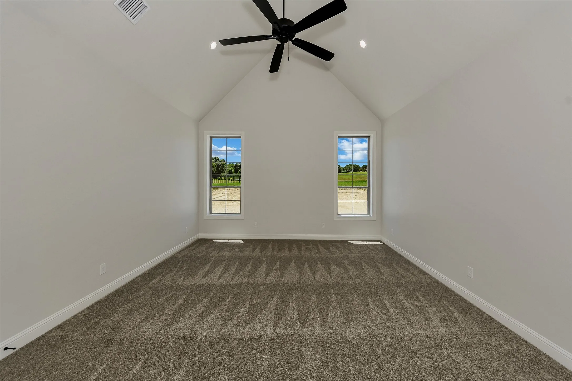 Spare room featuring dark colored carpet, a ceiling fan, and high vaulted ceiling