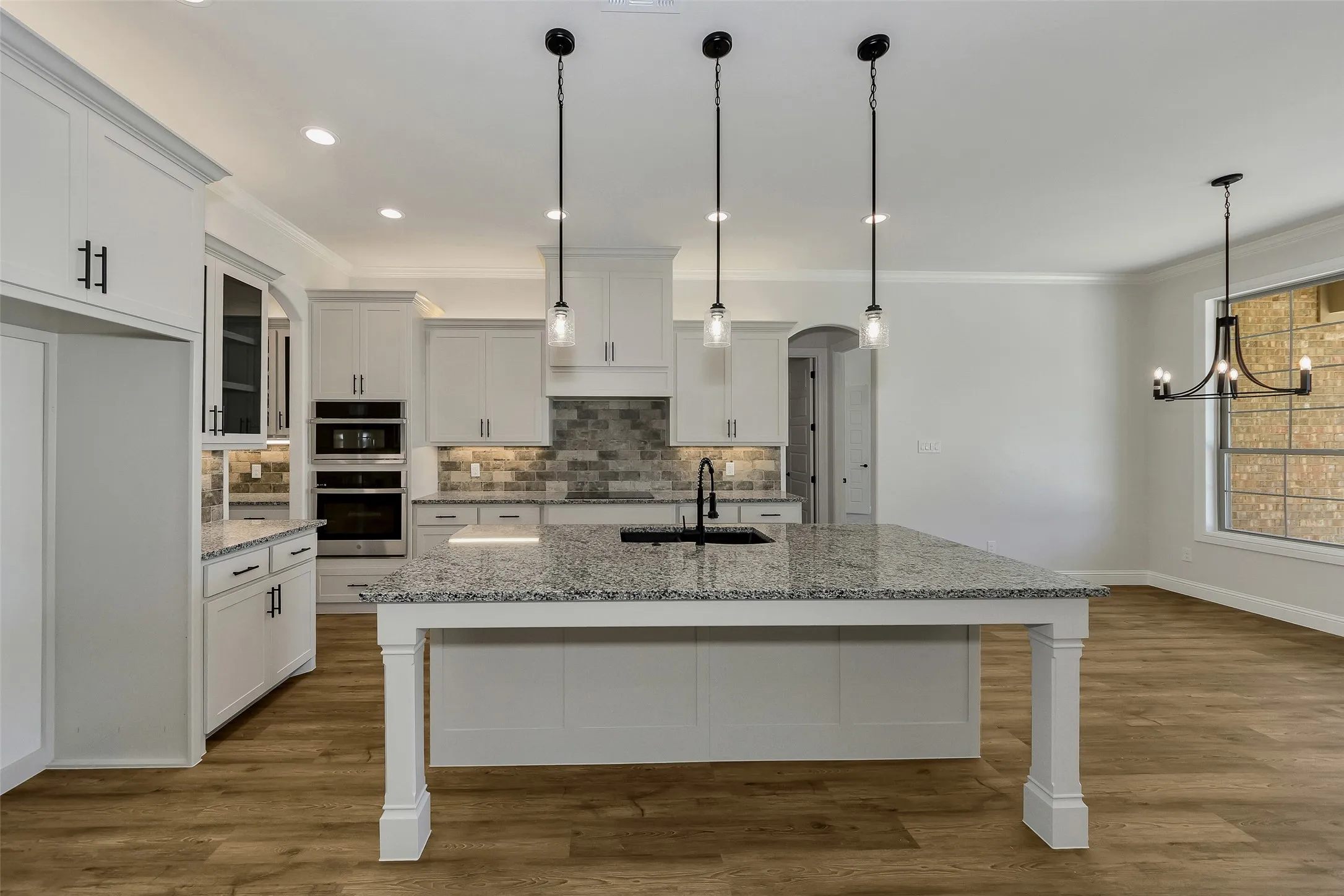 Kitchen featuring dark wood-style floors, crown molding, white cabinets, a breakfast bar area, and decorative backsplash