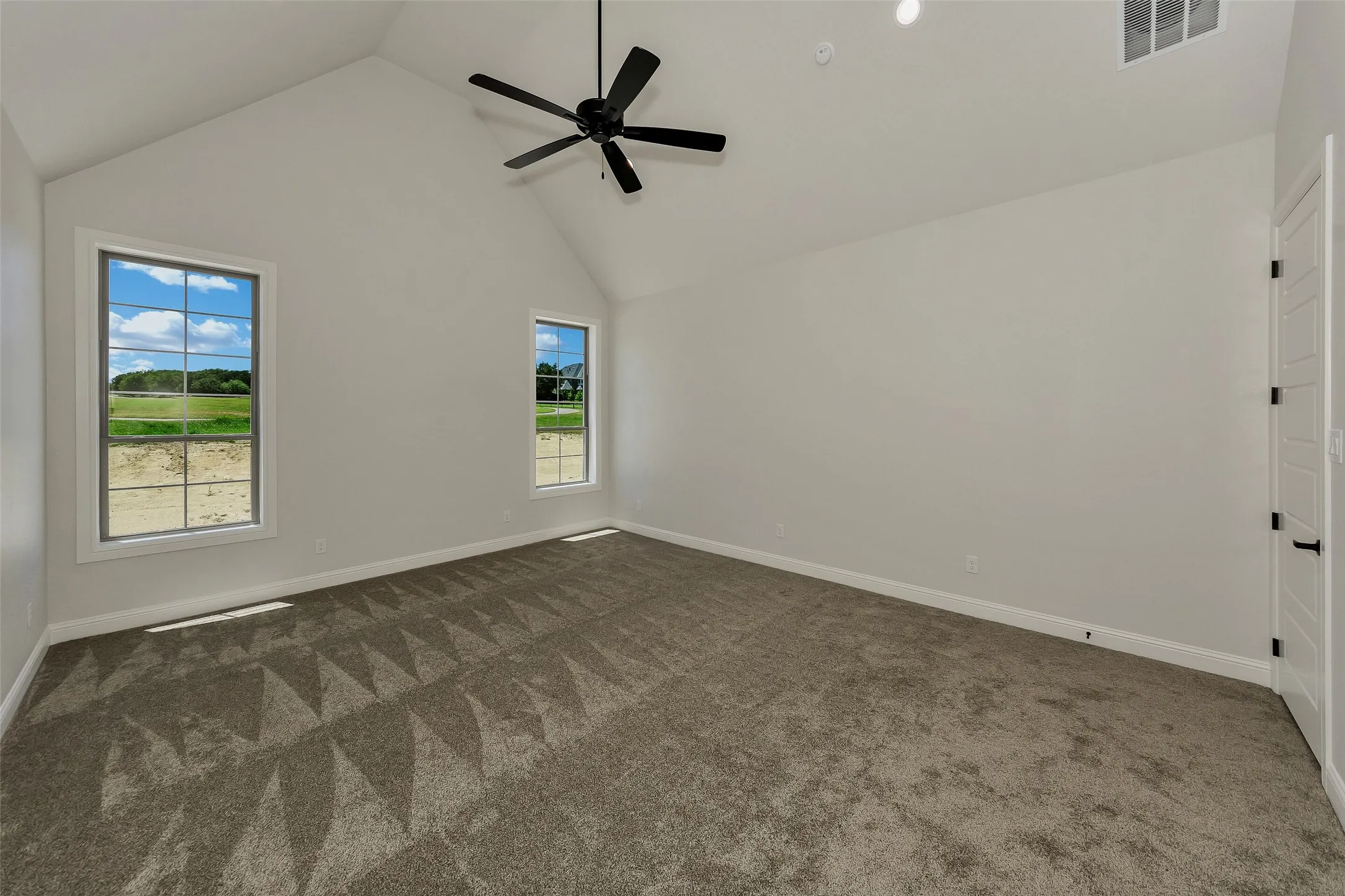 Unfurnished room featuring high vaulted ceiling, healthy amount of natural light, dark carpet, and a ceiling fan