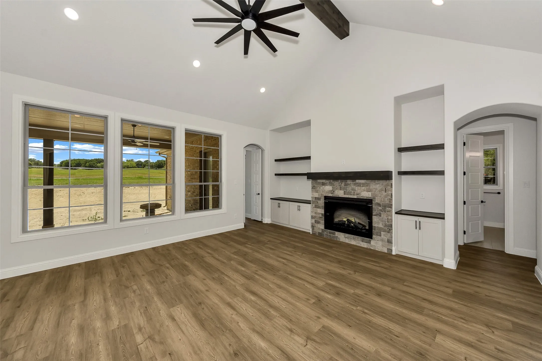 Unfurnished living room featuring healthy amount of natural light, a ceiling fan, arched walkways, beam ceiling, and wood finished floors