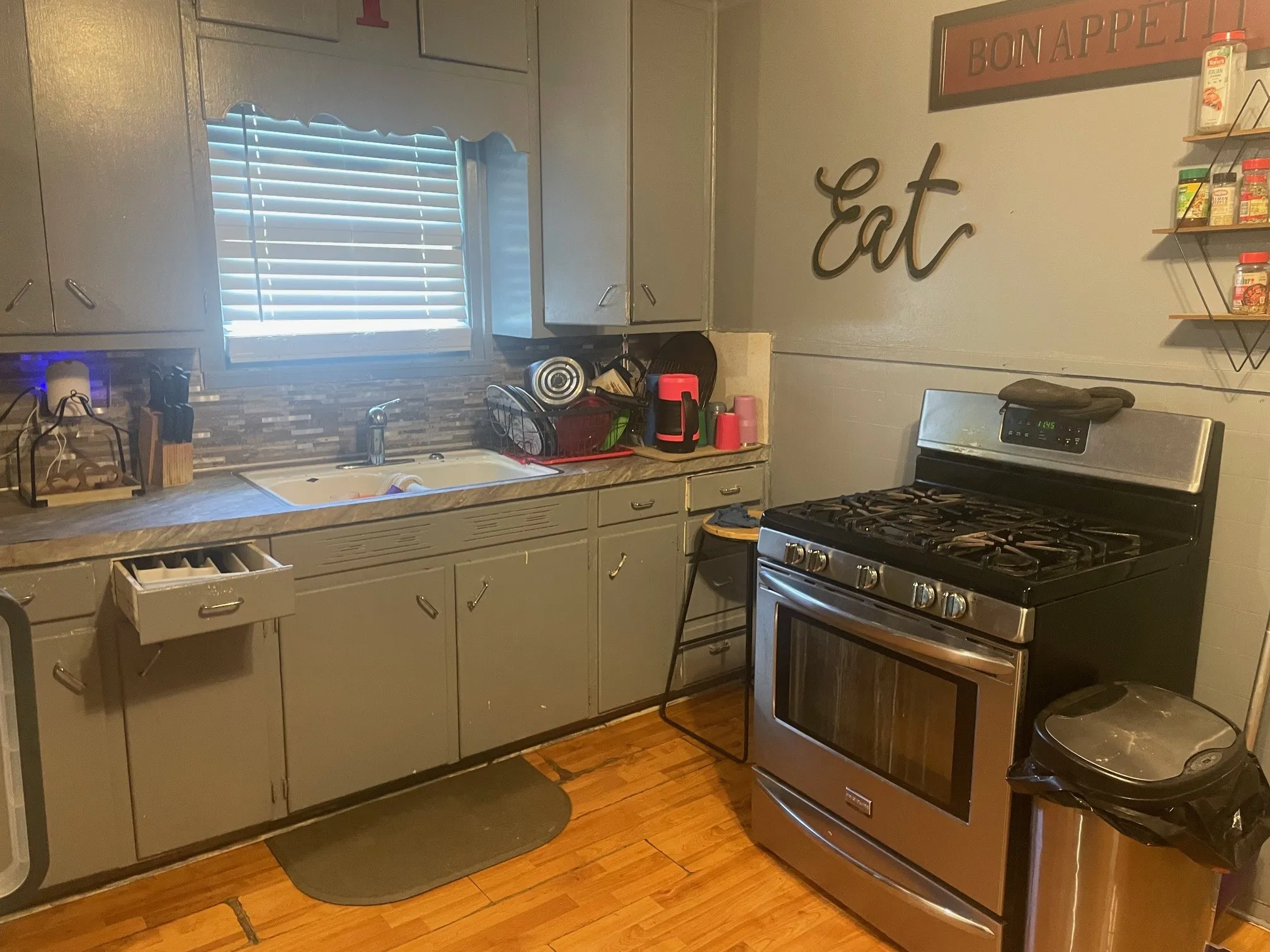 Kitchen featuring gas stove, light wood-style floors, tasteful backsplash, and dark countertops