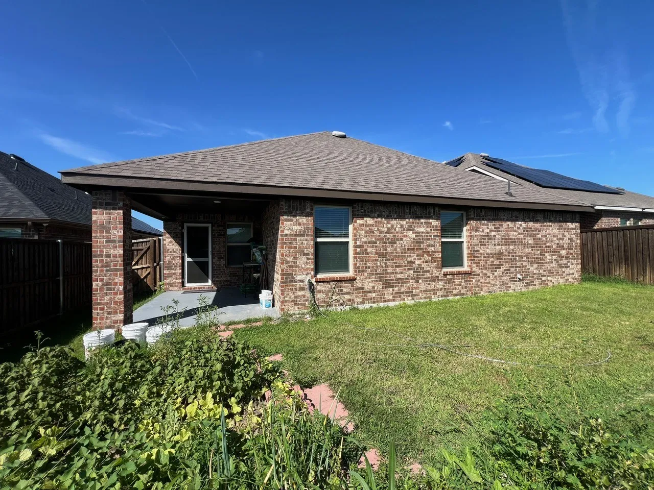 Back of house featuring roof with shingles, a fenced backyard, brick siding, and a patio area