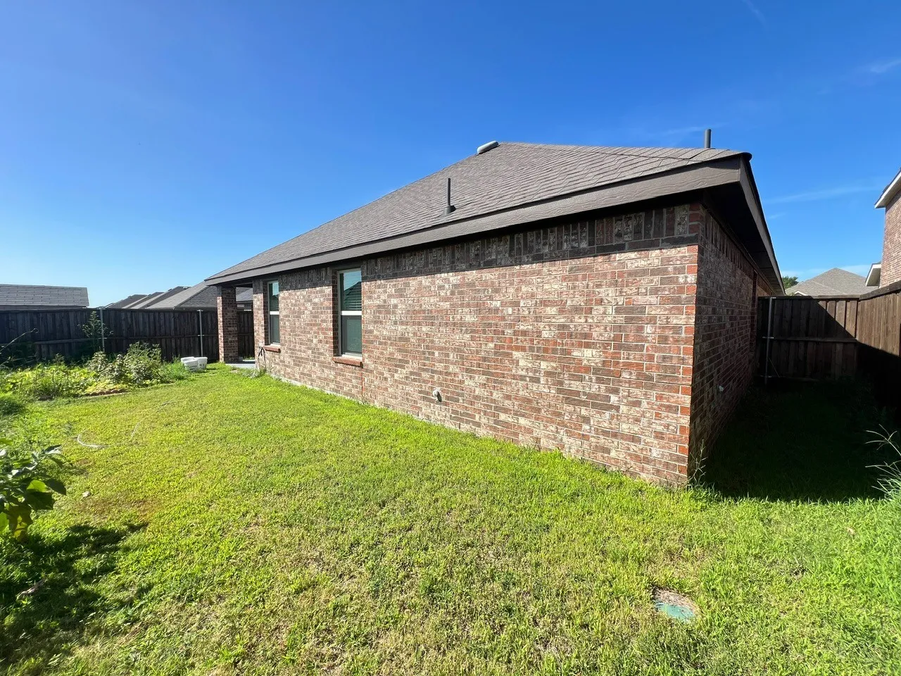 Back of house with brick siding, a fenced backyard, and roof with shingles