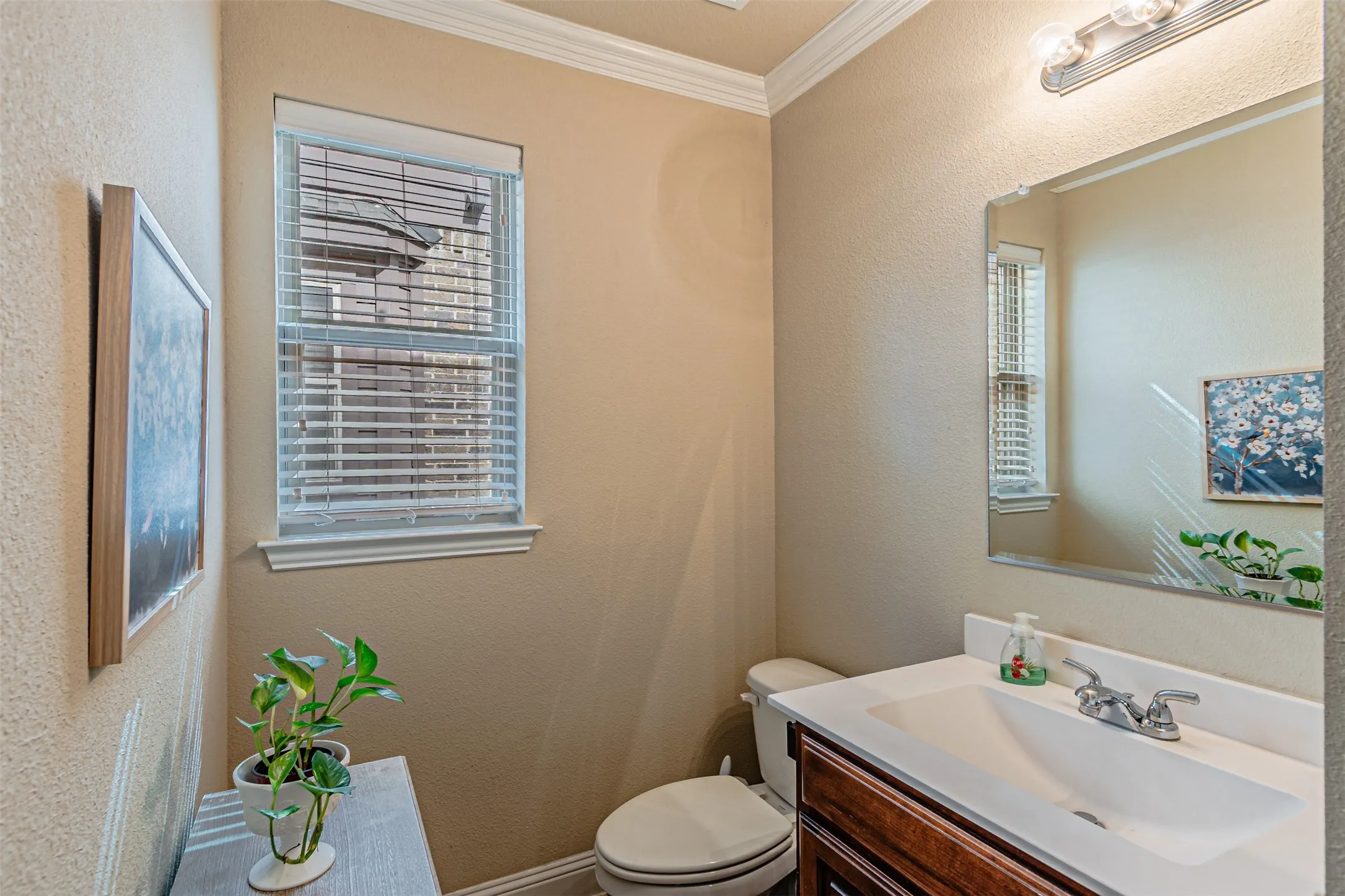 Half bathroom featuring a textured wall, crown molding, and vanity