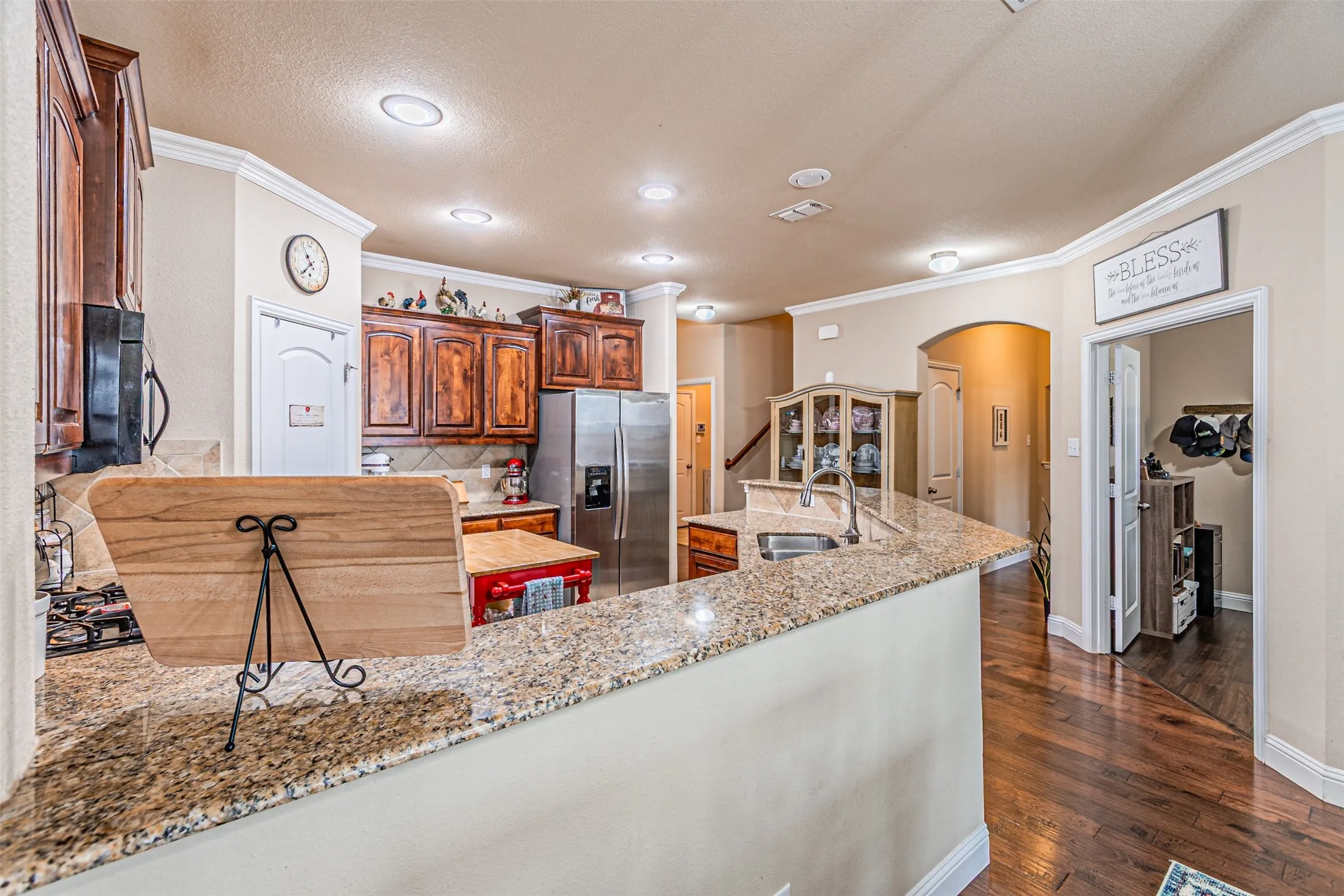 Kitchen featuring arched walkways, crown molding, stainless steel fridge, dark wood finished floors, and light stone countertops