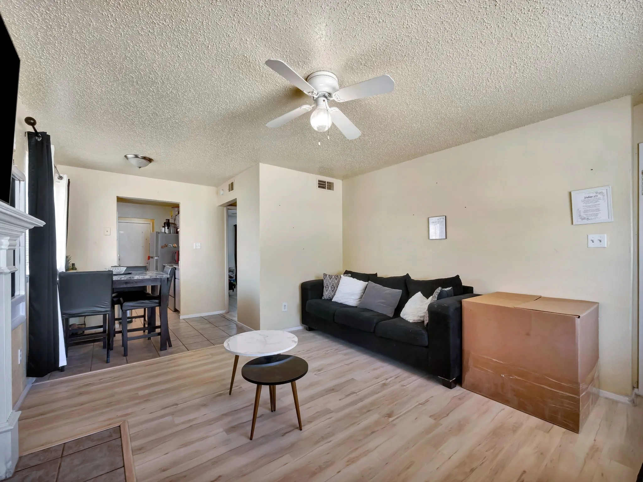Living area with a ceiling fan, a textured ceiling, and light wood finished floors