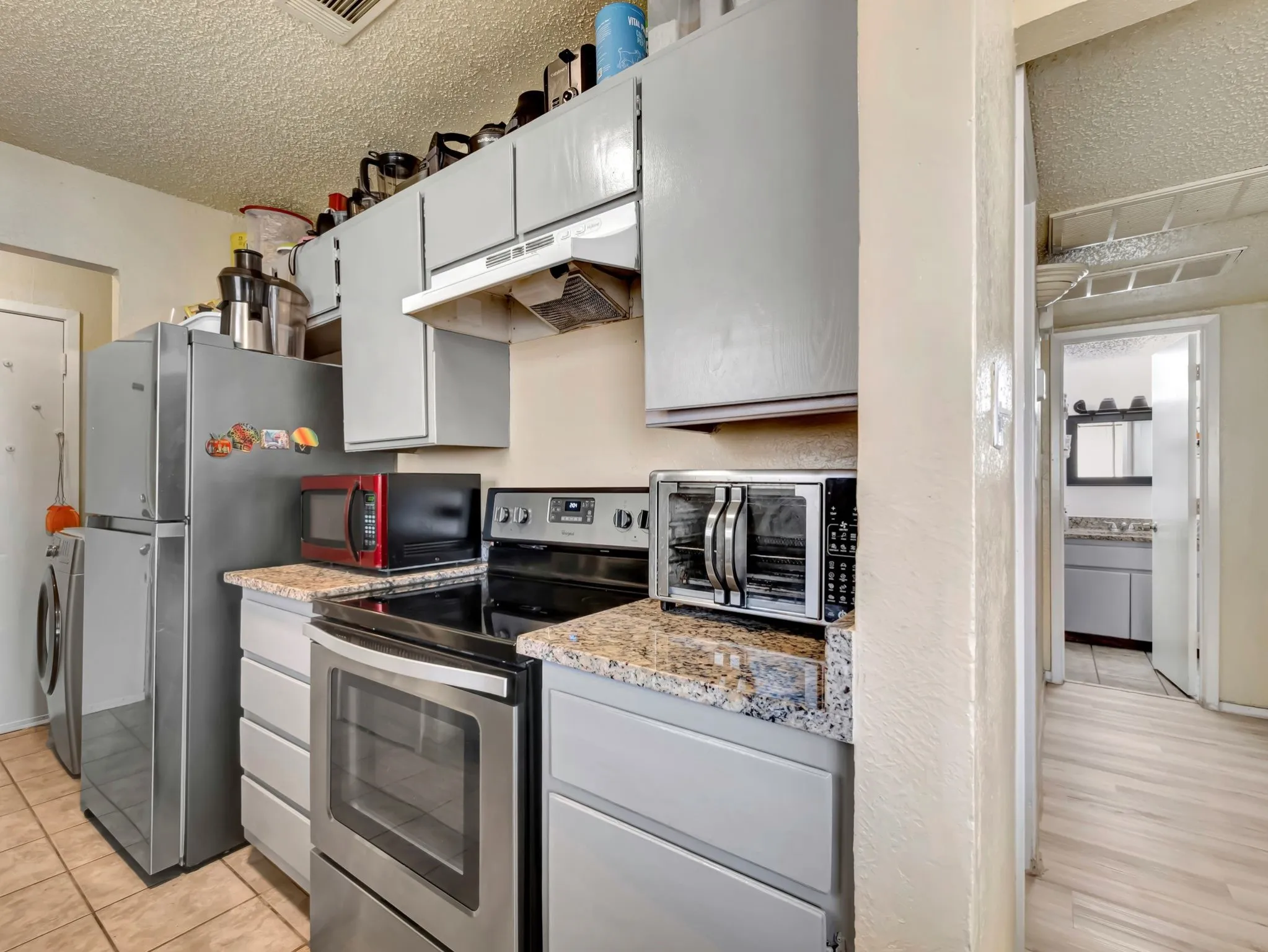 Kitchen with appliances with stainless steel finishes, a textured ceiling, under cabinet range hood, washing machine and clothes dryer, and light stone countertops