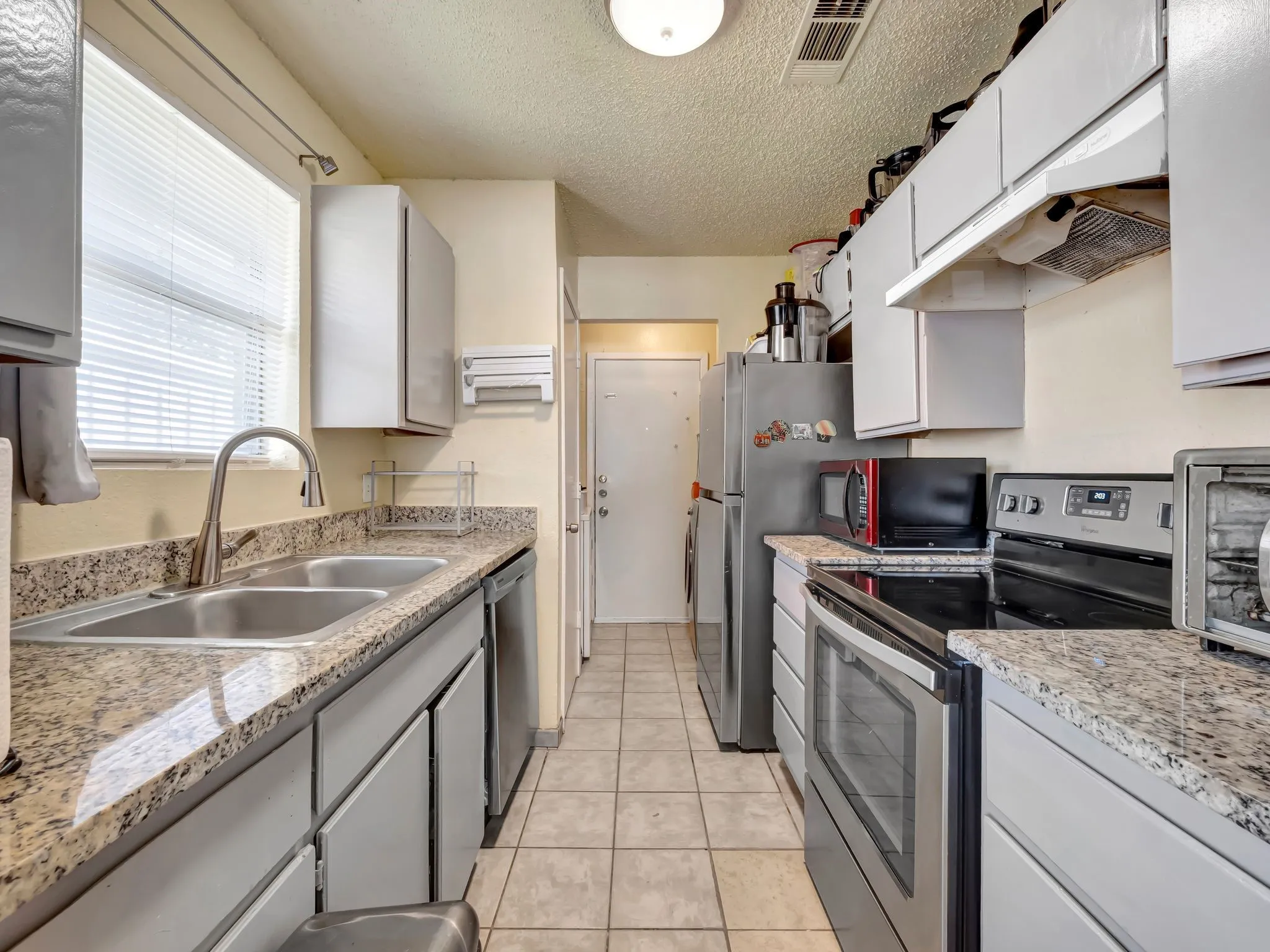 Kitchen featuring stainless steel appliances, a textured ceiling, under cabinet range hood, light tile patterned flooring, and white cabinetry
