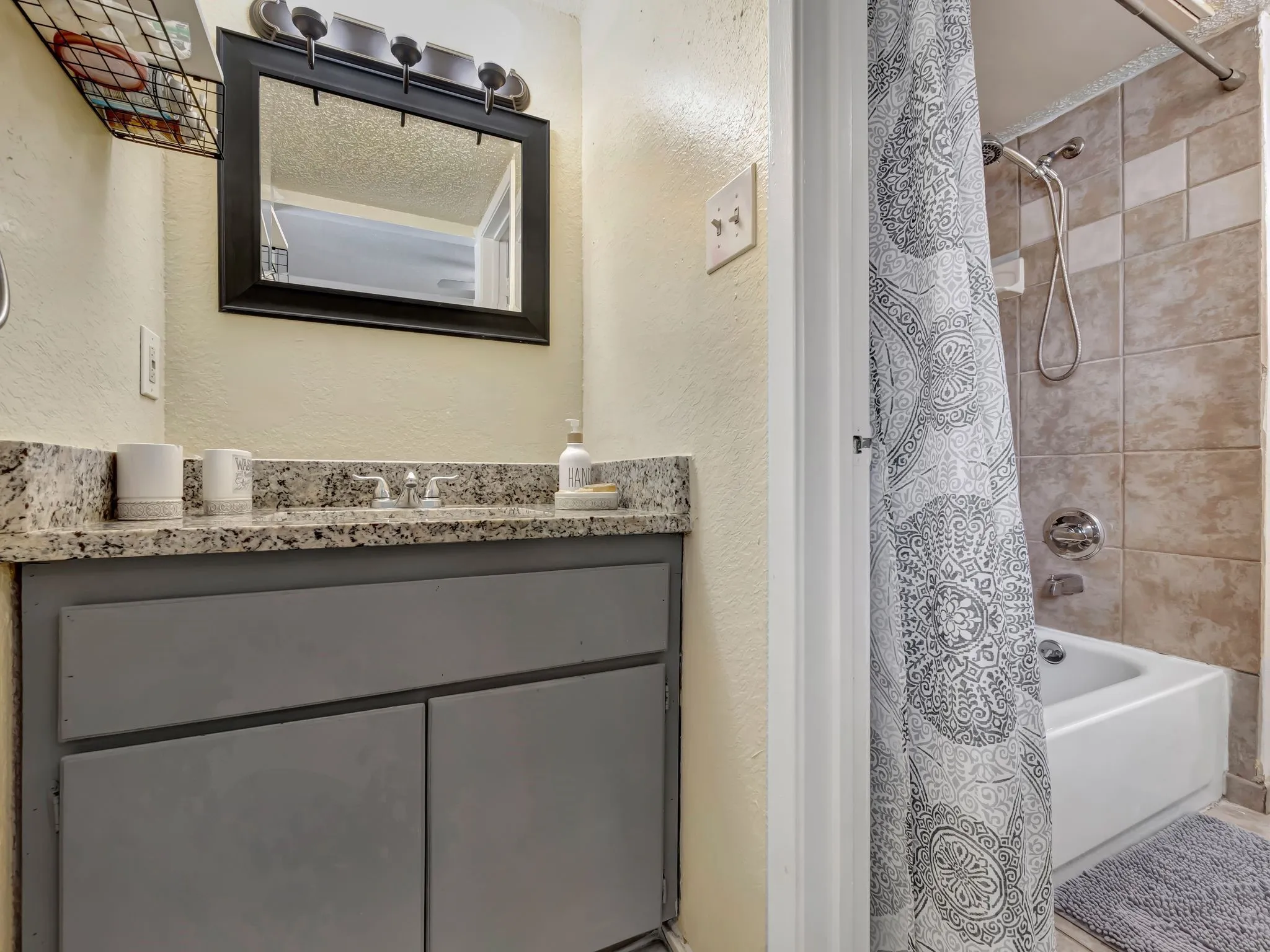 Full bathroom with a textured wall, vanity, and shower / bath combo with shower curtain