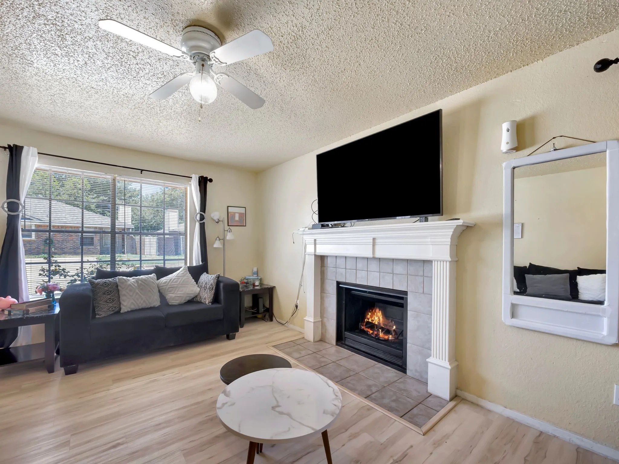 Living area with a tiled fireplace, a textured ceiling, wood finished floors, a ceiling fan, and a textured wall