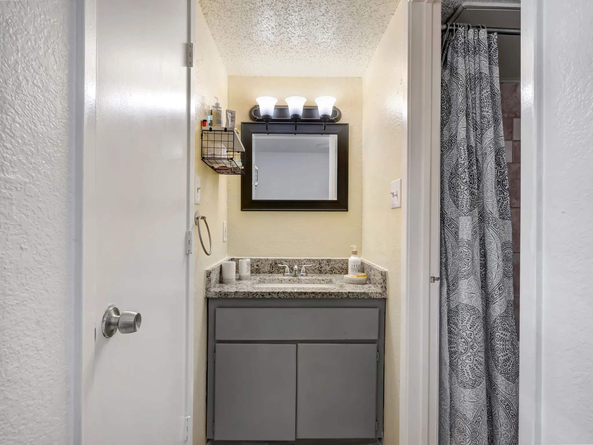 Bathroom with a textured wall, a textured ceiling, vanity, and curtained shower