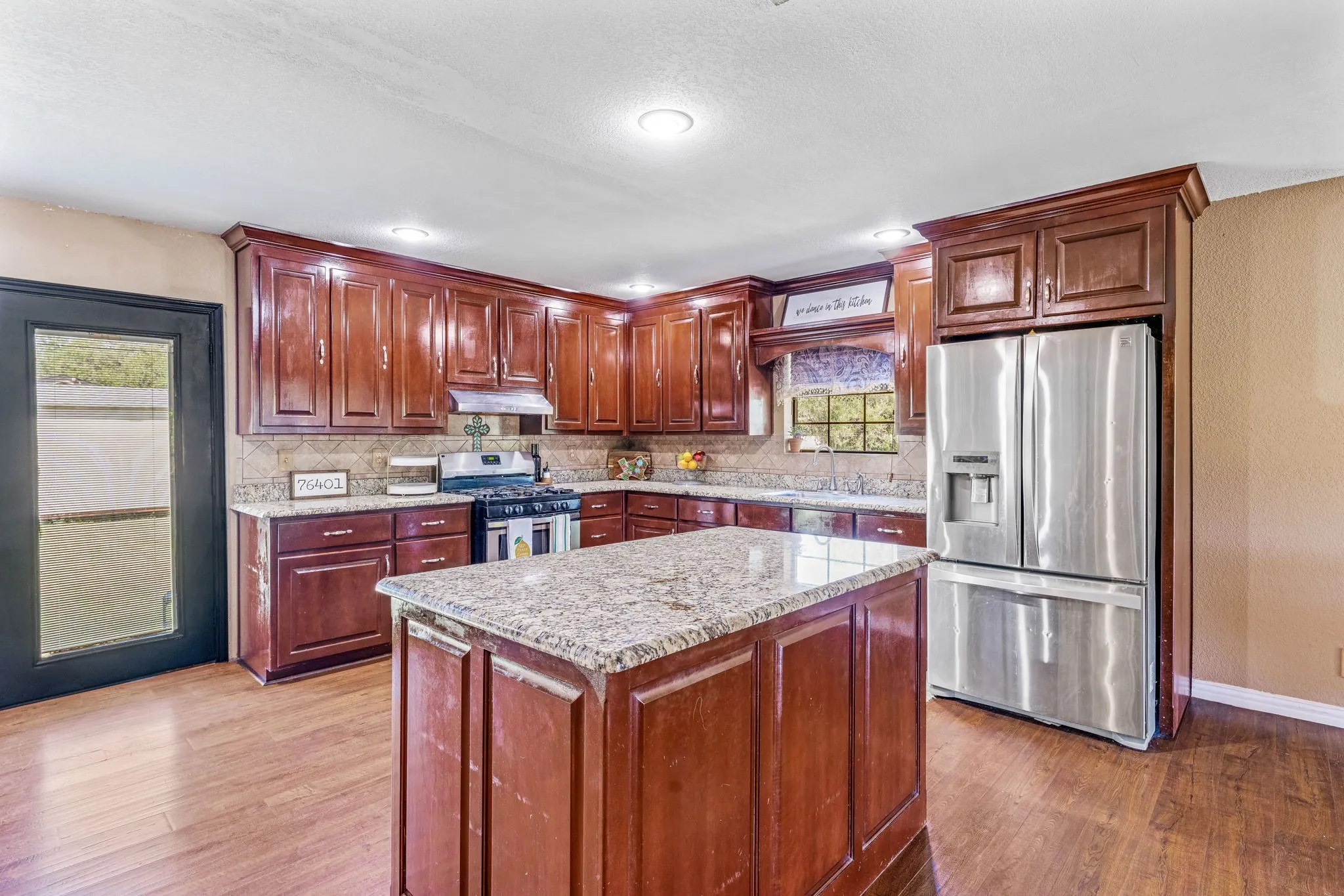 Kitchen featuring appliances with stainless steel finishes, tasteful backsplash, light wood finished floors, light stone countertops, and a textured ceiling