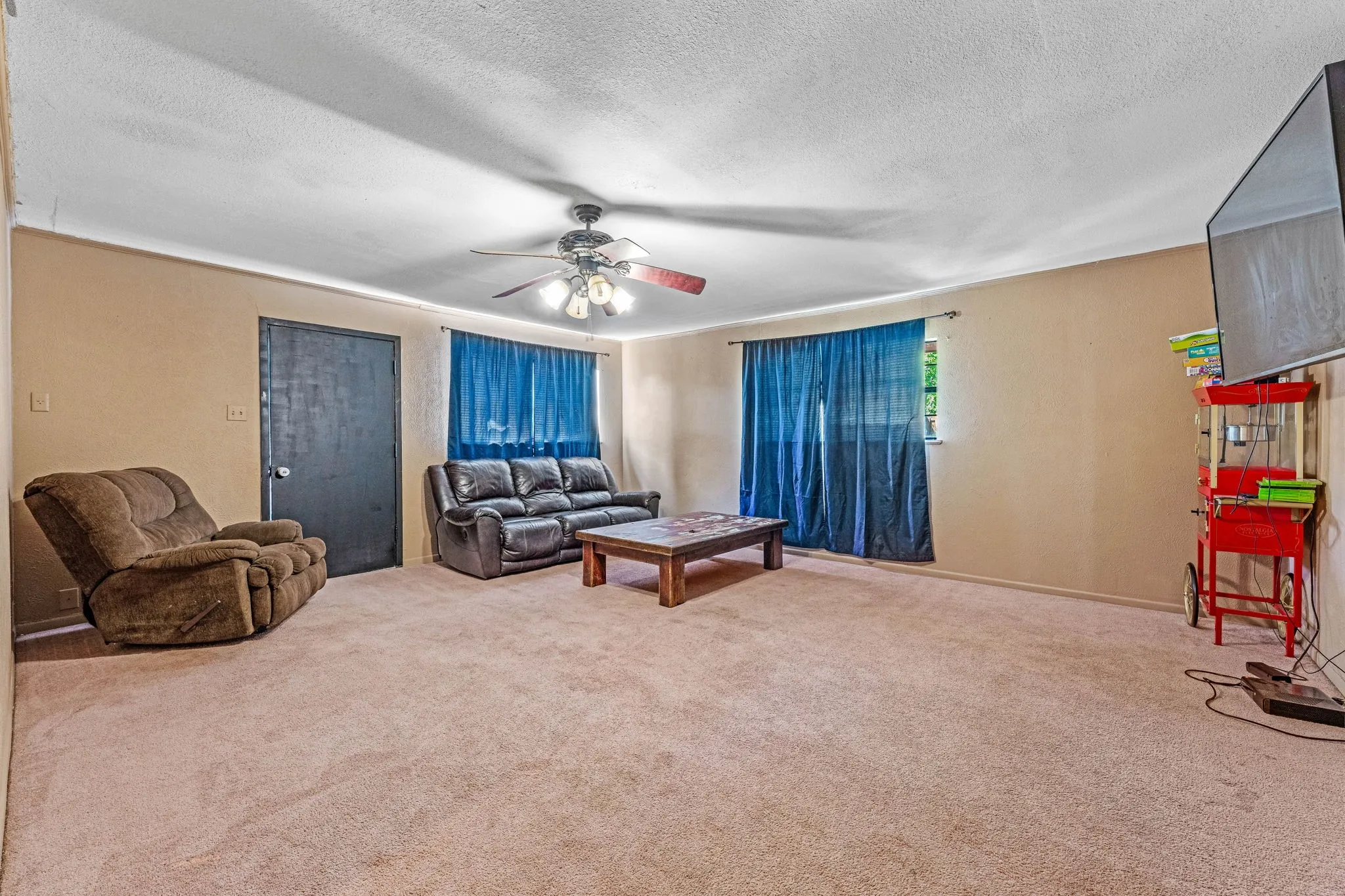 Carpeted living area with a ceiling fan and a textured ceiling