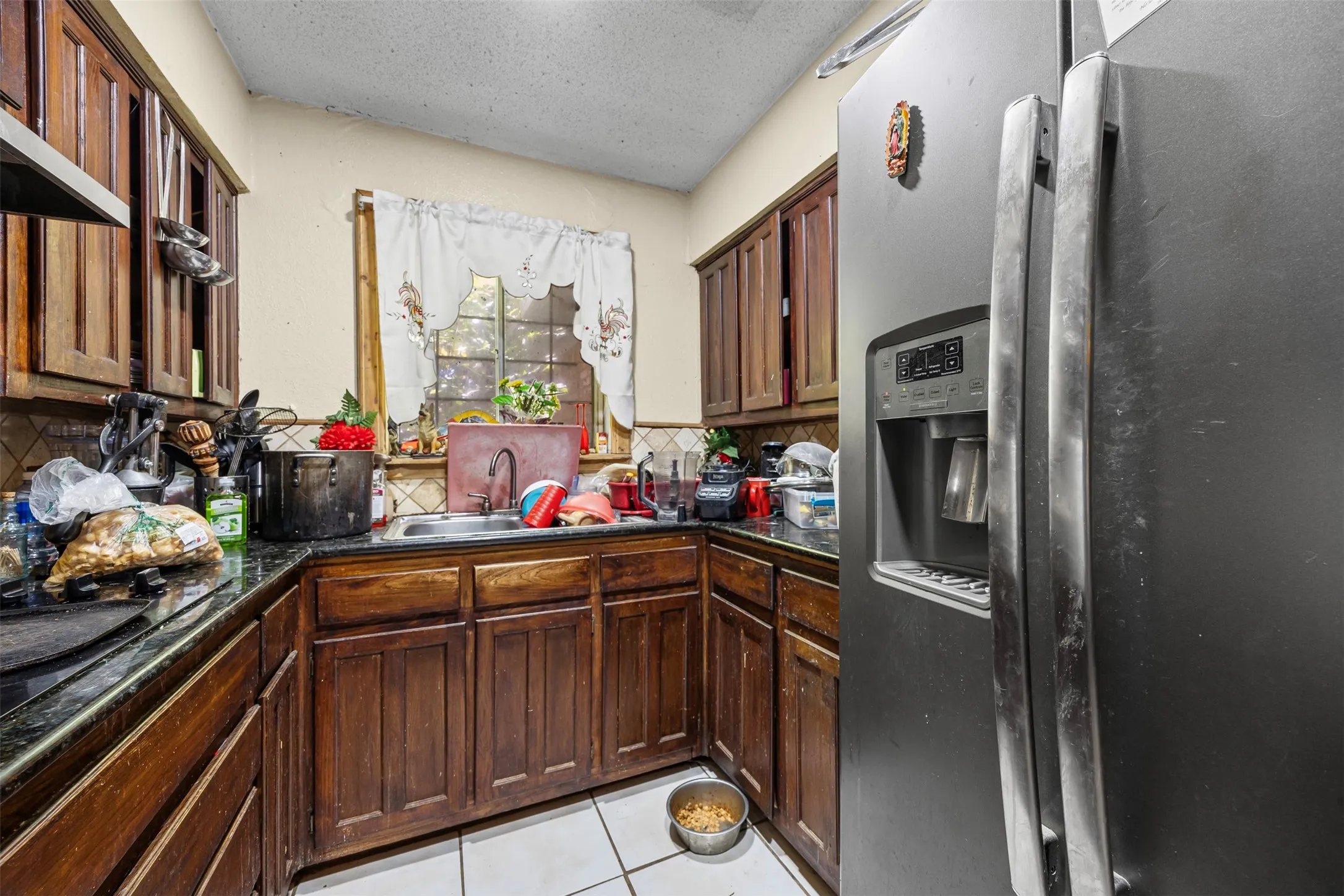 Kitchen with stainless steel fridge with ice dispenser, decorative backsplash, a textured ceiling, light tile patterned floors, and dark countertops