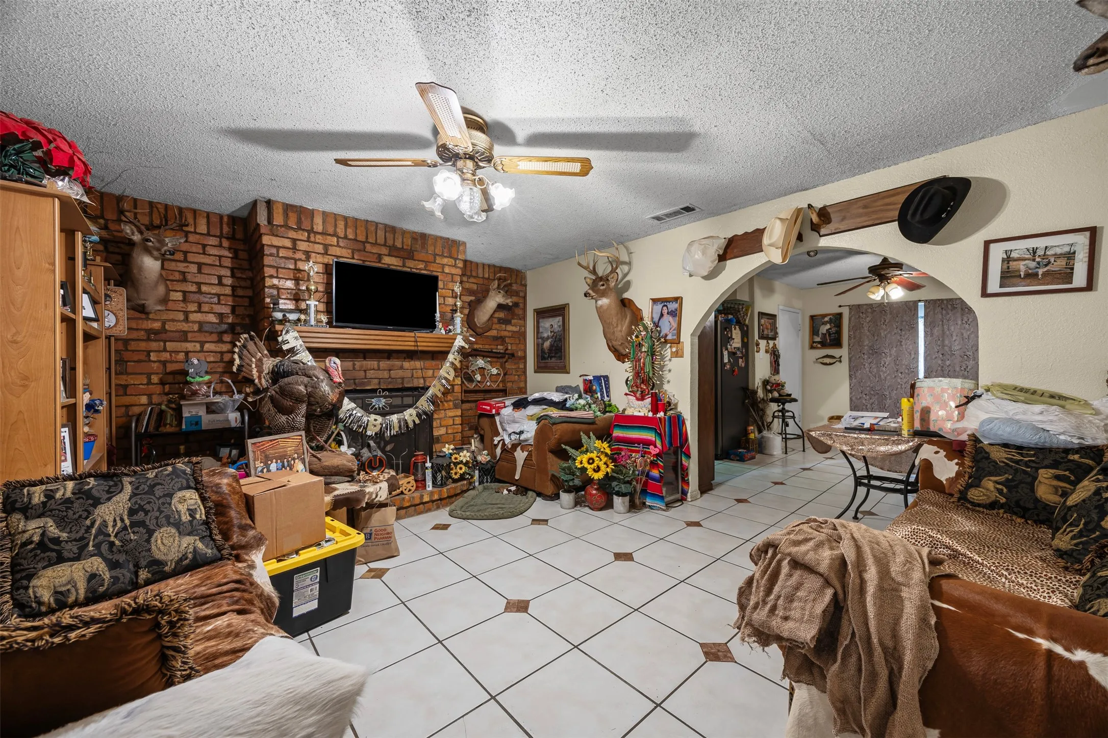 Living room featuring ceiling fan, a textured ceiling, arched walkways, a fireplace, and light tile patterned floors
