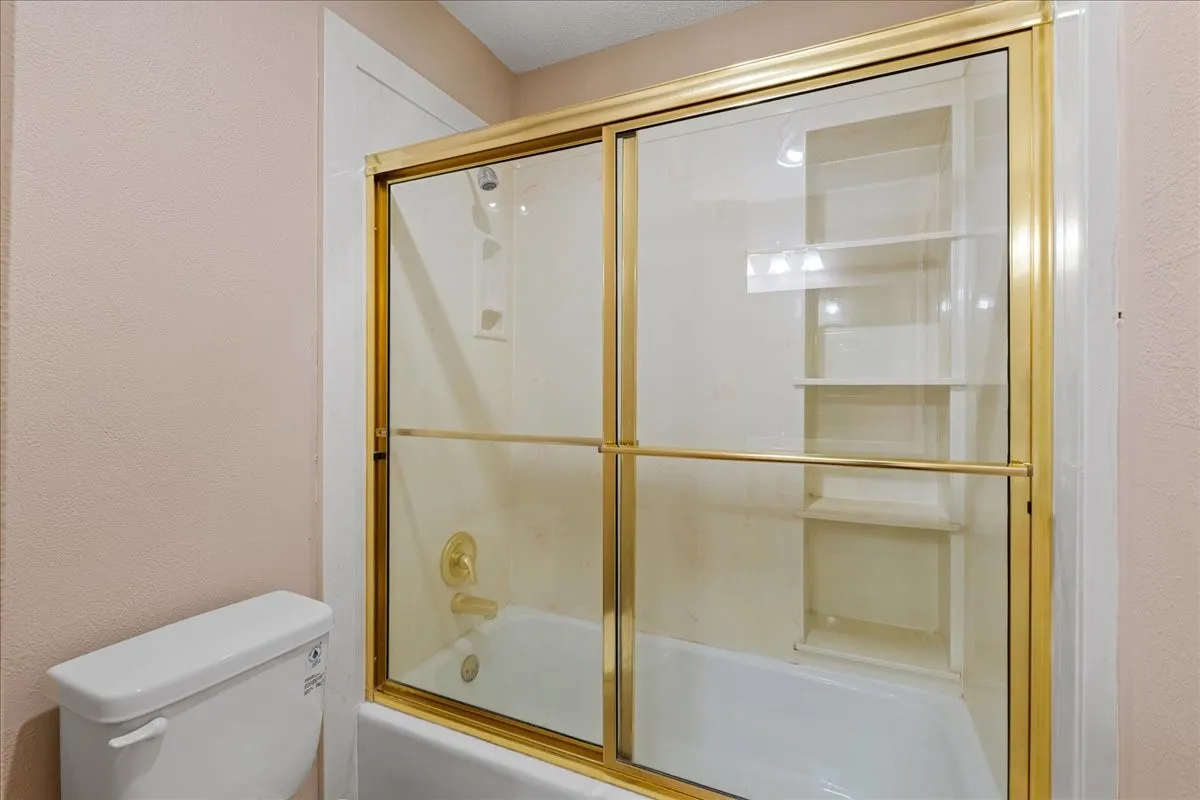 Bathroom with a textured wall and bath / shower combo with glass door