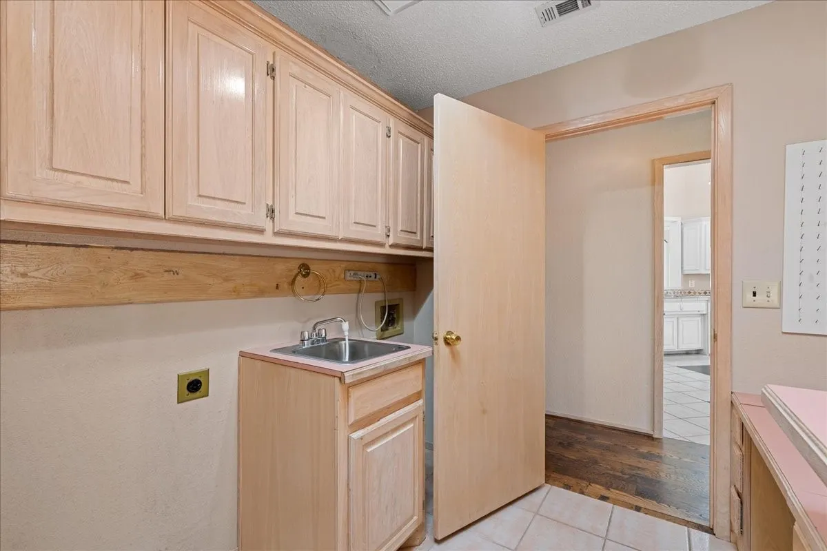 Washroom with hookup for an electric dryer, cabinet space, light tile patterned floors, a textured ceiling, and hookup for a washing machine