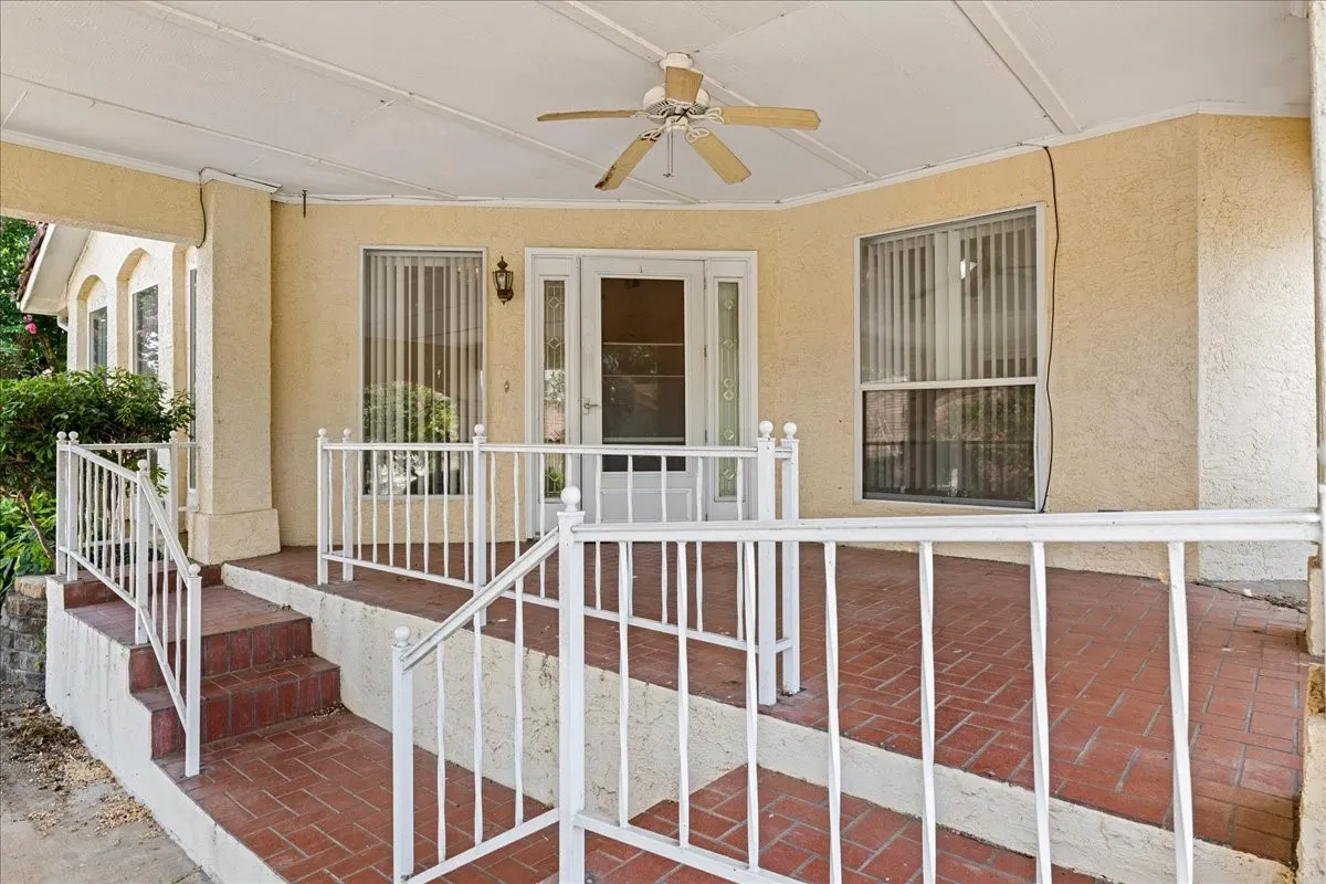 Doorway to property featuring ceiling fan, stucco siding, and covered porch