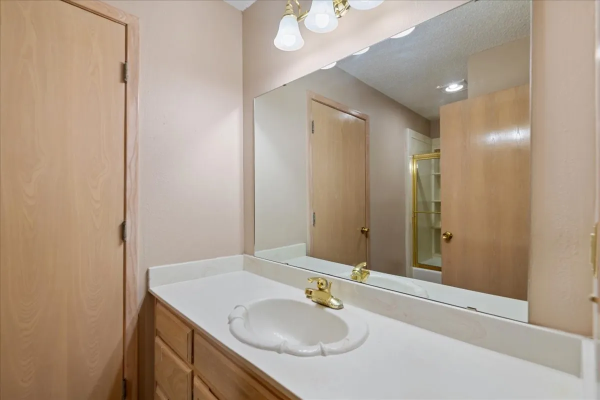 Full bath featuring a textured ceiling, vanity, and combined bath / shower with glass door