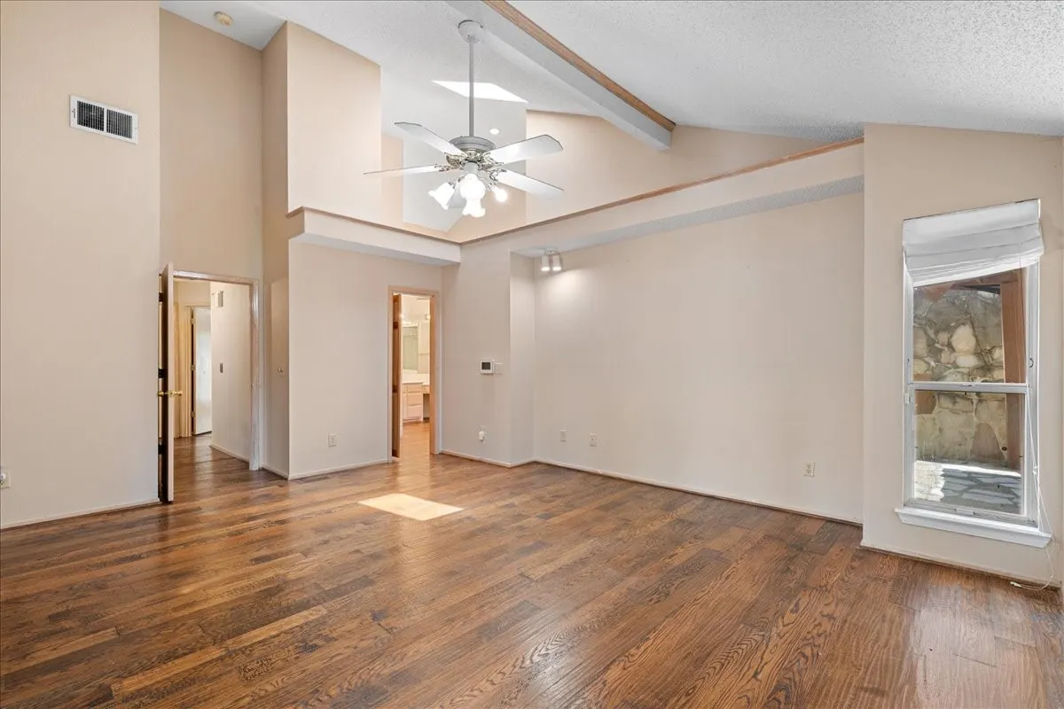 Unfurnished room with wood finished floors, beamed ceiling, a ceiling fan, high vaulted ceiling, and a textured ceiling
