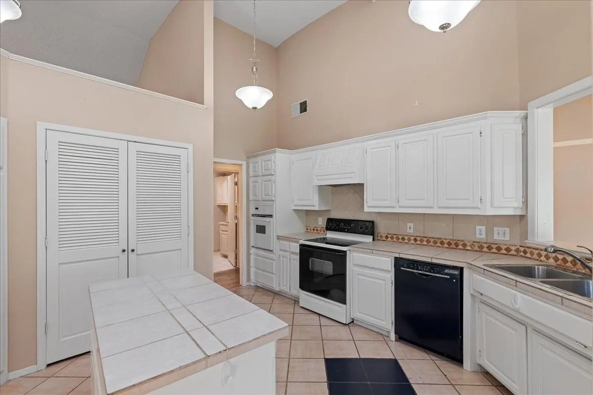 Kitchen featuring high vaulted ceiling, tile countertops, white appliances, light tile patterned floors, and decorative backsplash