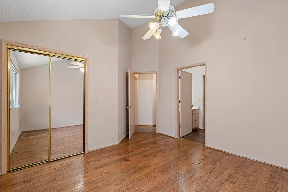 Unfurnished bedroom with wood finished floors, high vaulted ceiling, a closet, connected bathroom, and a ceiling fan