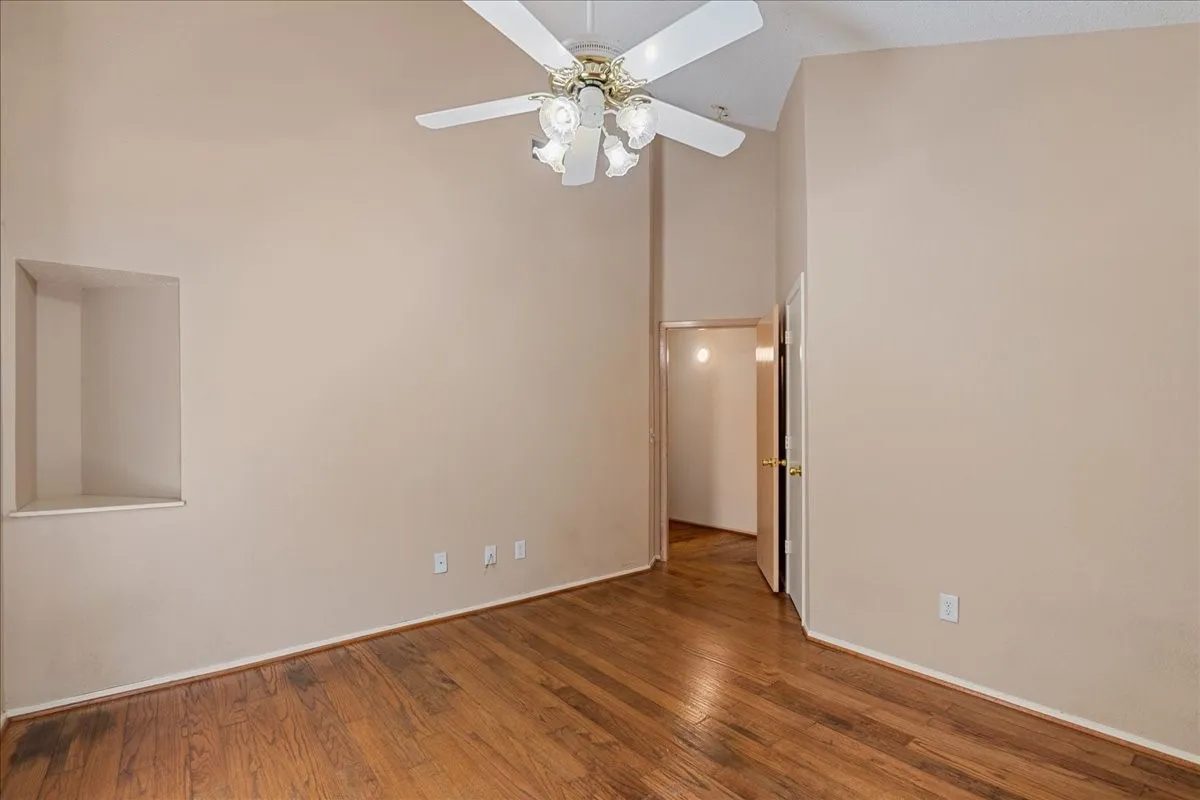 Empty room featuring a high ceiling, wood finished floors, and a ceiling fan