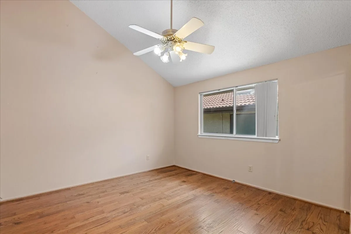 Empty room with lofted ceiling, a textured ceiling, wood finished floors, and ceiling fan