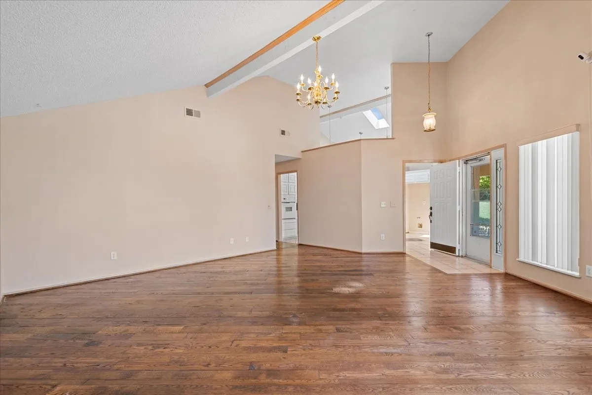Unfurnished living room featuring hardwood / wood-style flooring, plenty of natural light, beam ceiling, a chandelier, and high vaulted ceiling