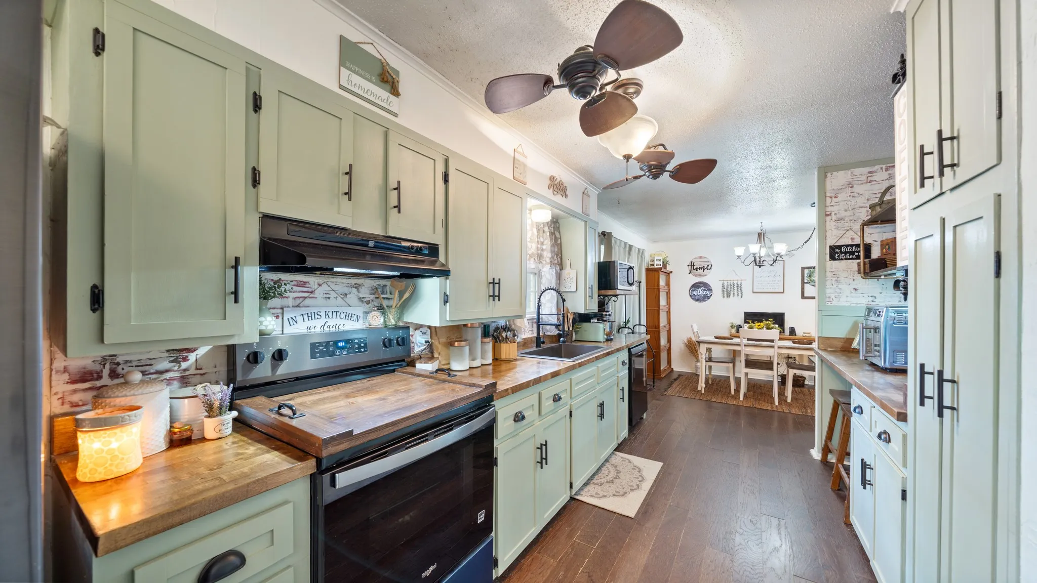 Green cabinetry with black hardware, wood-finish countertops, stainless steel range and range hood, and wood-finish flooring