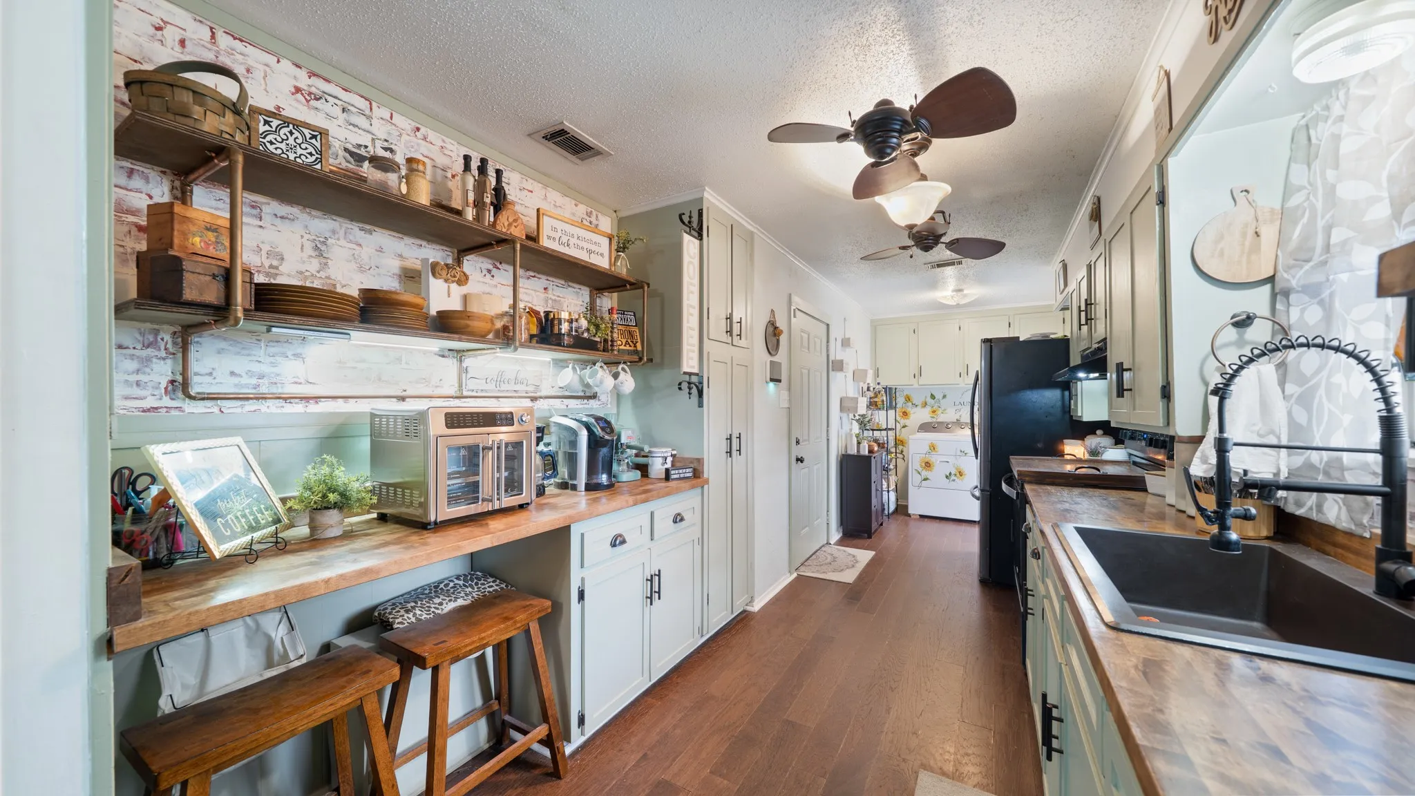 Wood-finish flooring, exposed brick-style accent wall, open shelving, ceiling fans, and a built-in sink with a matte black faucet