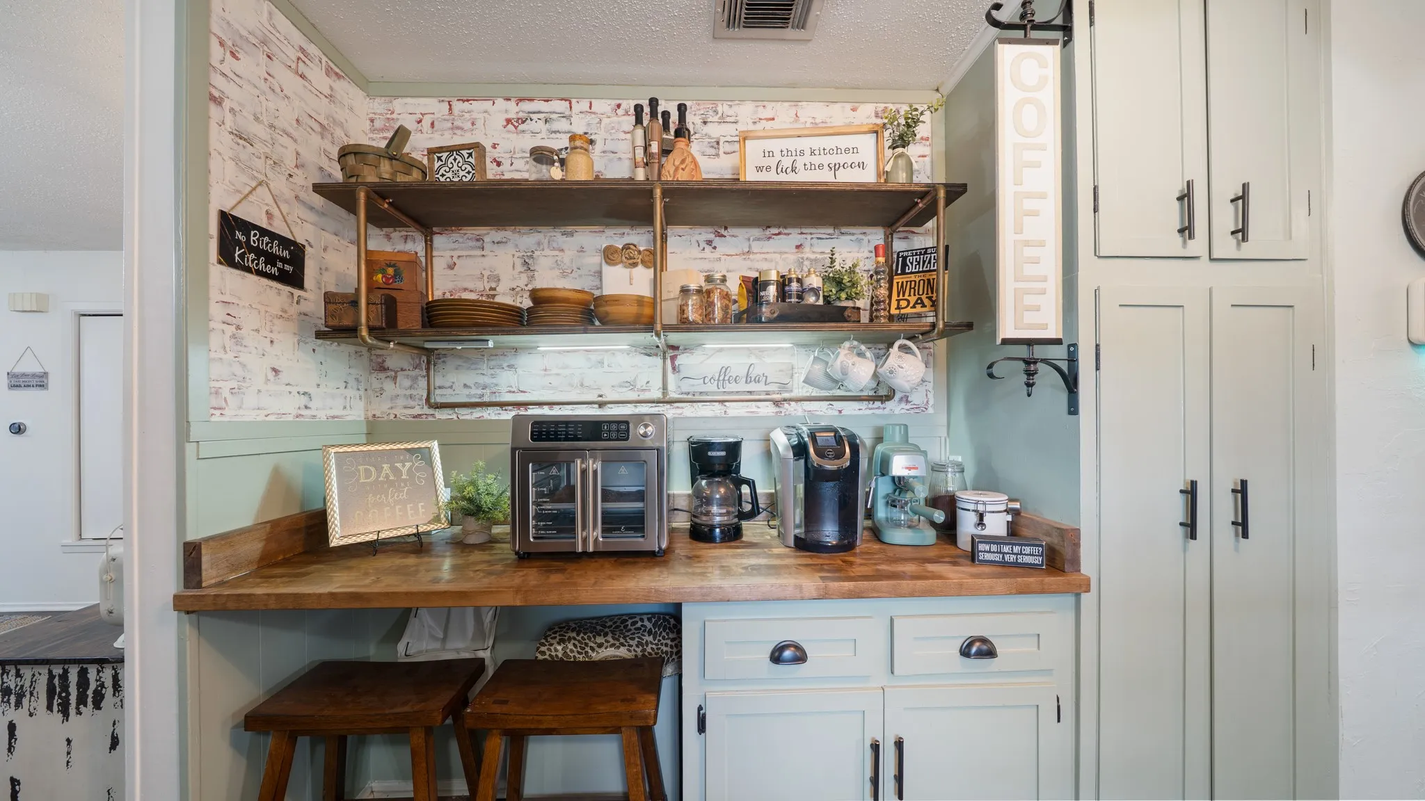 Wood-finish countertop with light green cabinetry, open shelving, and brick-patterned wall covering