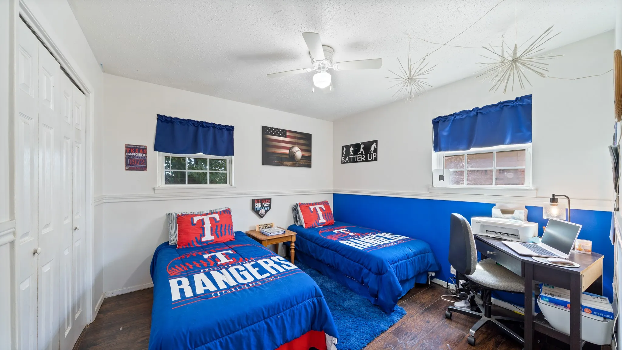 White paneled bi-fold closet doors, two windows with white trim, wood-finish flooring, and a ceiling fan